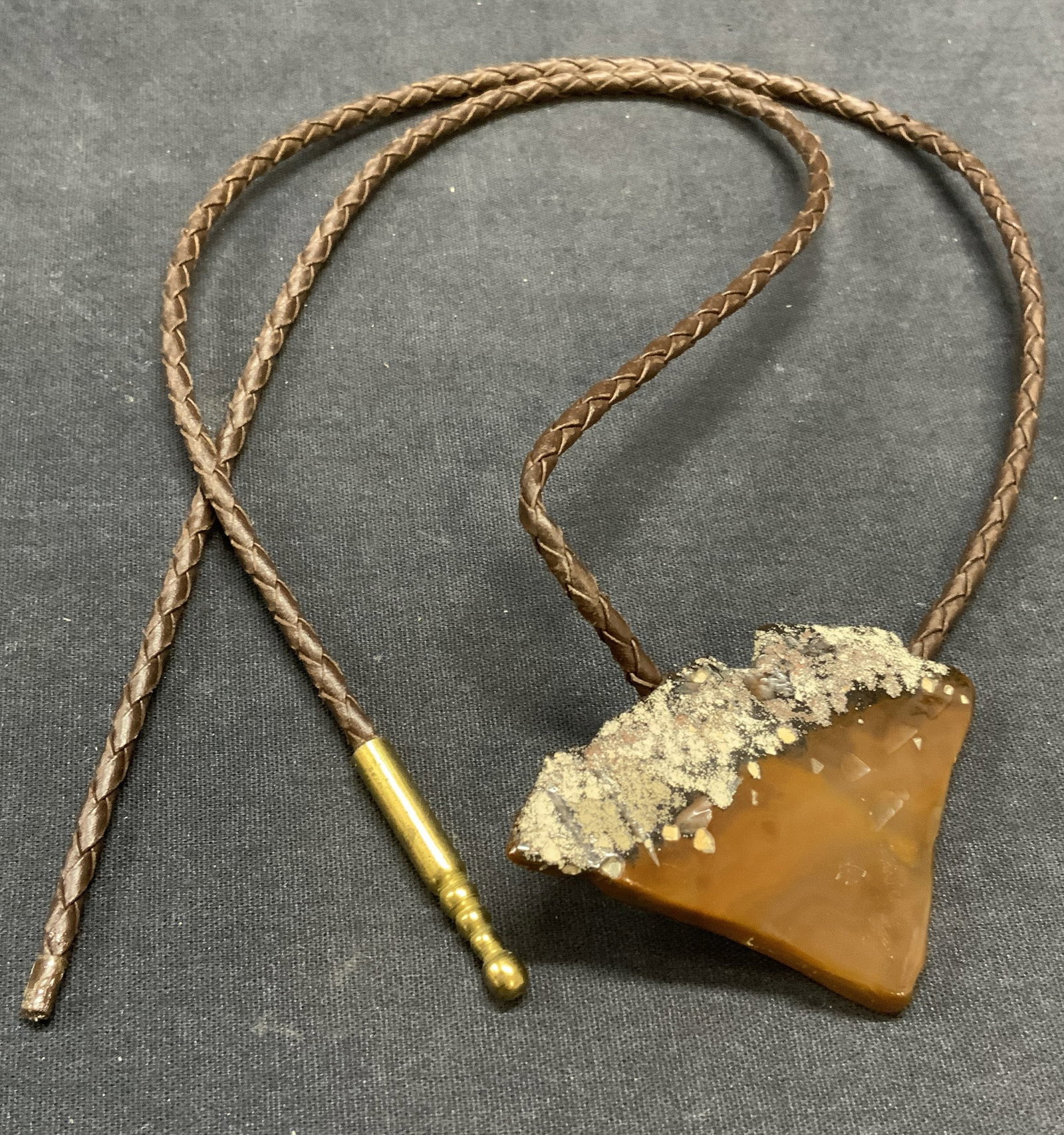 Brown Leather & Stone Bolo Tie Necklace: Vintage brown woven leather cord and brown stone bolo tie necklace. Drop length approx. 16 inches. Some surface wear including scratching observed. 1 cap needs replacement. Estate jewelry, costume jew