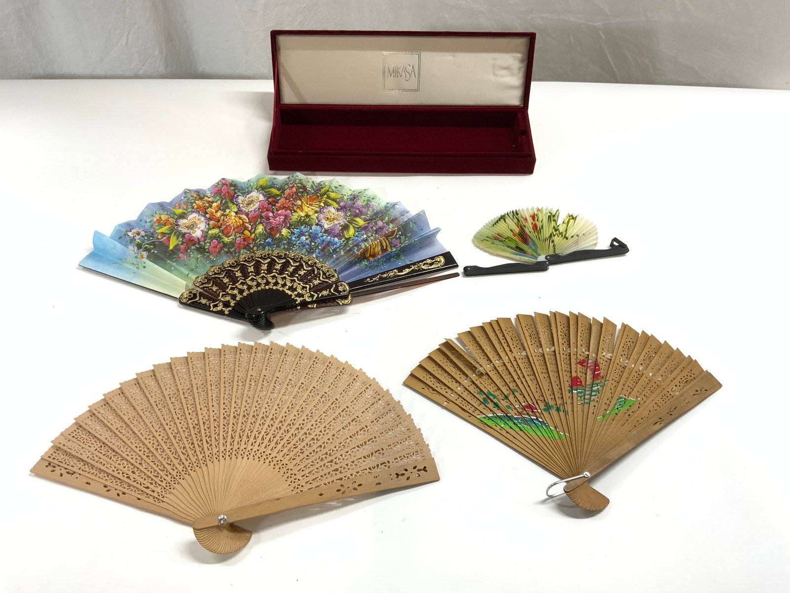 Lot 5 MIKASA Lidded Case & Hand Fans: Lot includes 4 hand fans and 1 lidded case trademarked MIKASA. Case is lined in red toned crushed velvet. One hand fan has intricate multi toned floral and leaf detail, w black & gold toned gilt detai