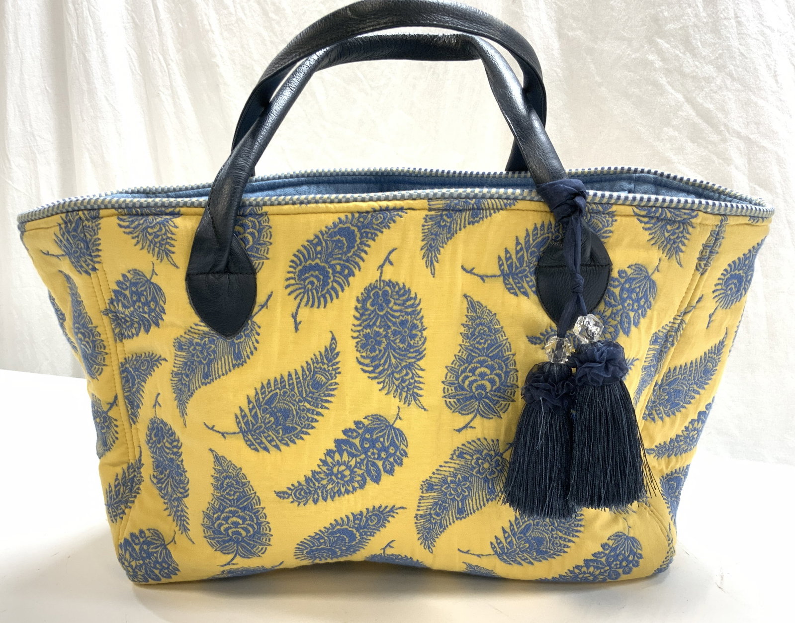 BagDazzled Embroidered Cotton Carry All Tote: Large tote bag, yellow with embroidered blue leaves. Large decorative tassels hang from the thick leather handles. Interior is all blue denim with several quick grab pockets. Zippered closure. Thick p