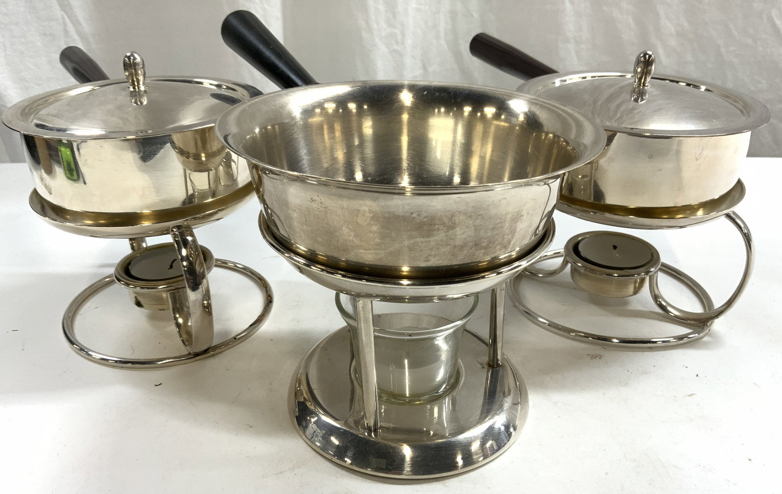 SPRING 3 Fondue Pots W Candles, Stands & Lids: Lot includes 3 fondue pots. Undersides of 2 are inscribed SPRING, 2 include lids. Each have black or dark brown toned handles which appear to possibly be Ebonized wood. Each pot includes metal stand &