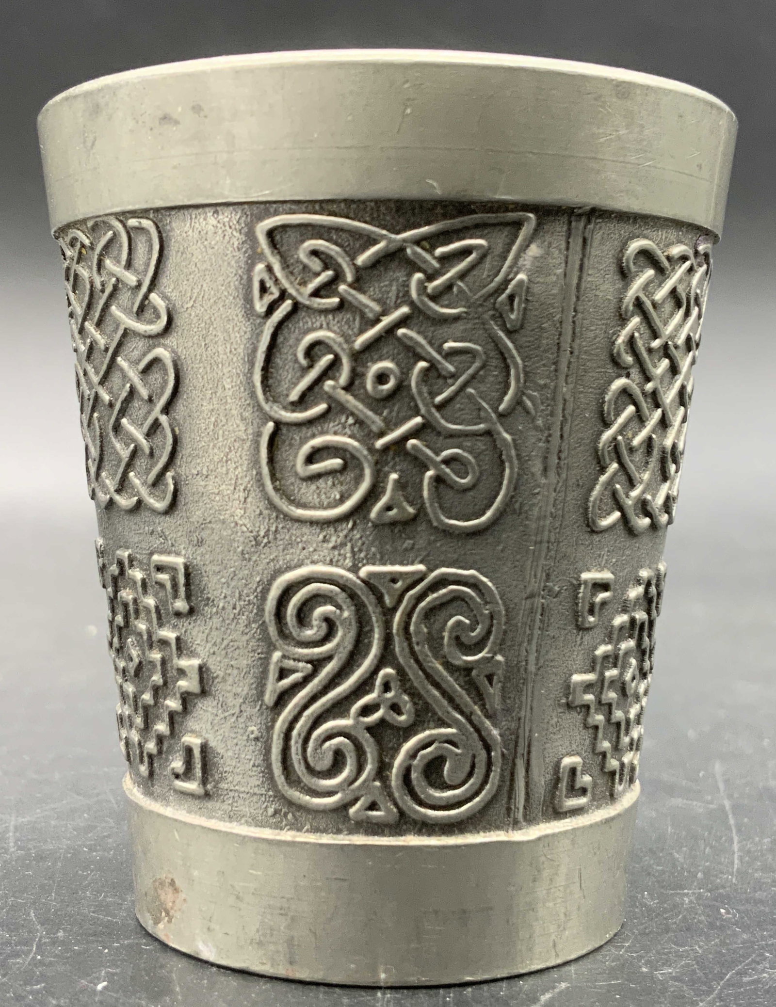 MULLINGAR IRELAND Vintage Metal Shot Glass: A vintage silver tone metal shot glass. Raised geometric patterns to the sides. Underside reads MADE IN MULLINGAR IRELAND. Measures approx. 2.25H x 2W in. Some surface wear consistent with age and use