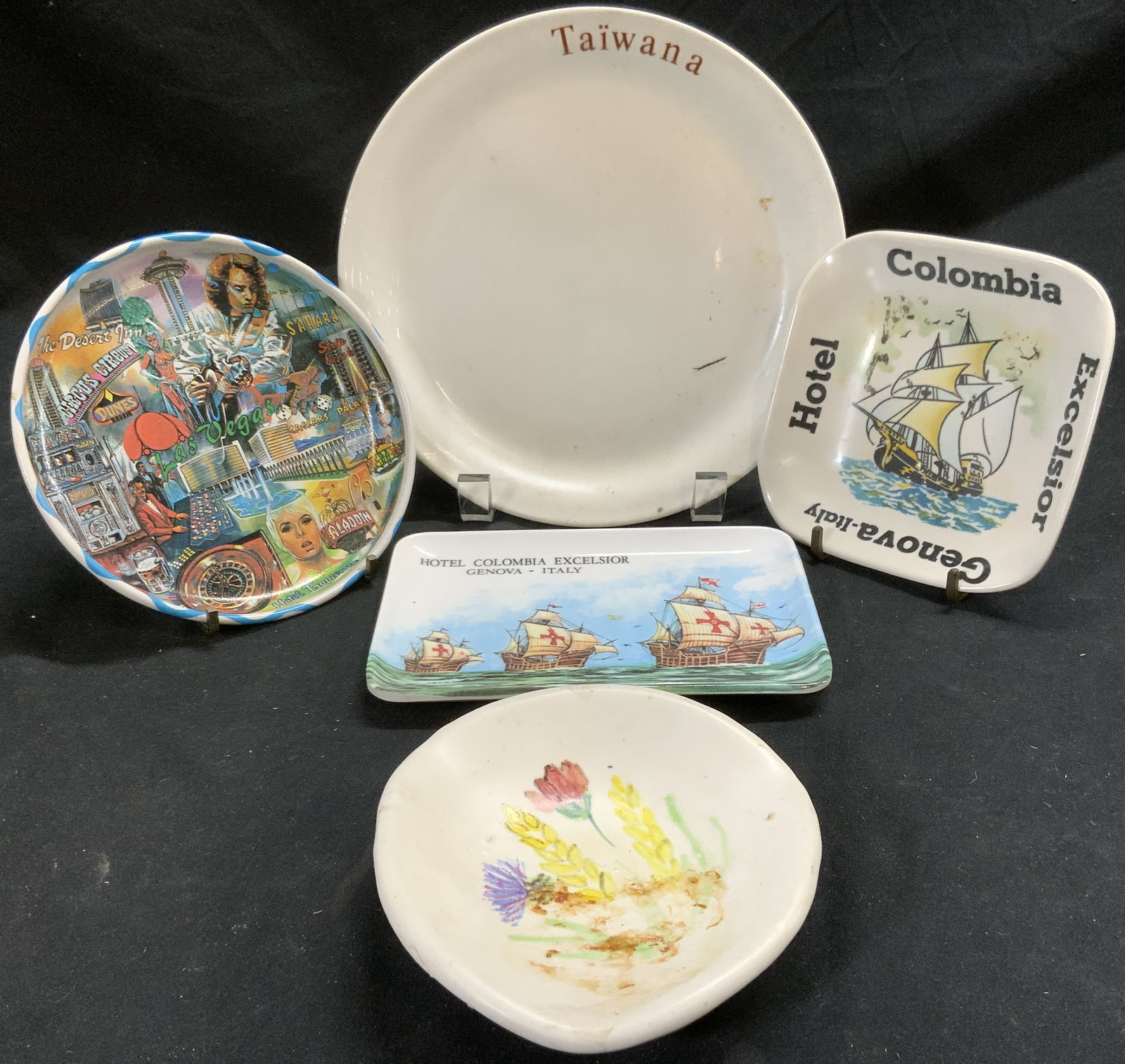 Lot 5 Vintage Plates Dishes Italy, Las Vegas, More: Lot includes 1 porcelain plate marked TAIWANA, 1 Hand painted trinket dish with floral and leaf detail, 1 tray depicting ships which reads HOTEL COLOMBIA EXCELSIOR GENOVA ITALY, 1 dish depicting 1 shi