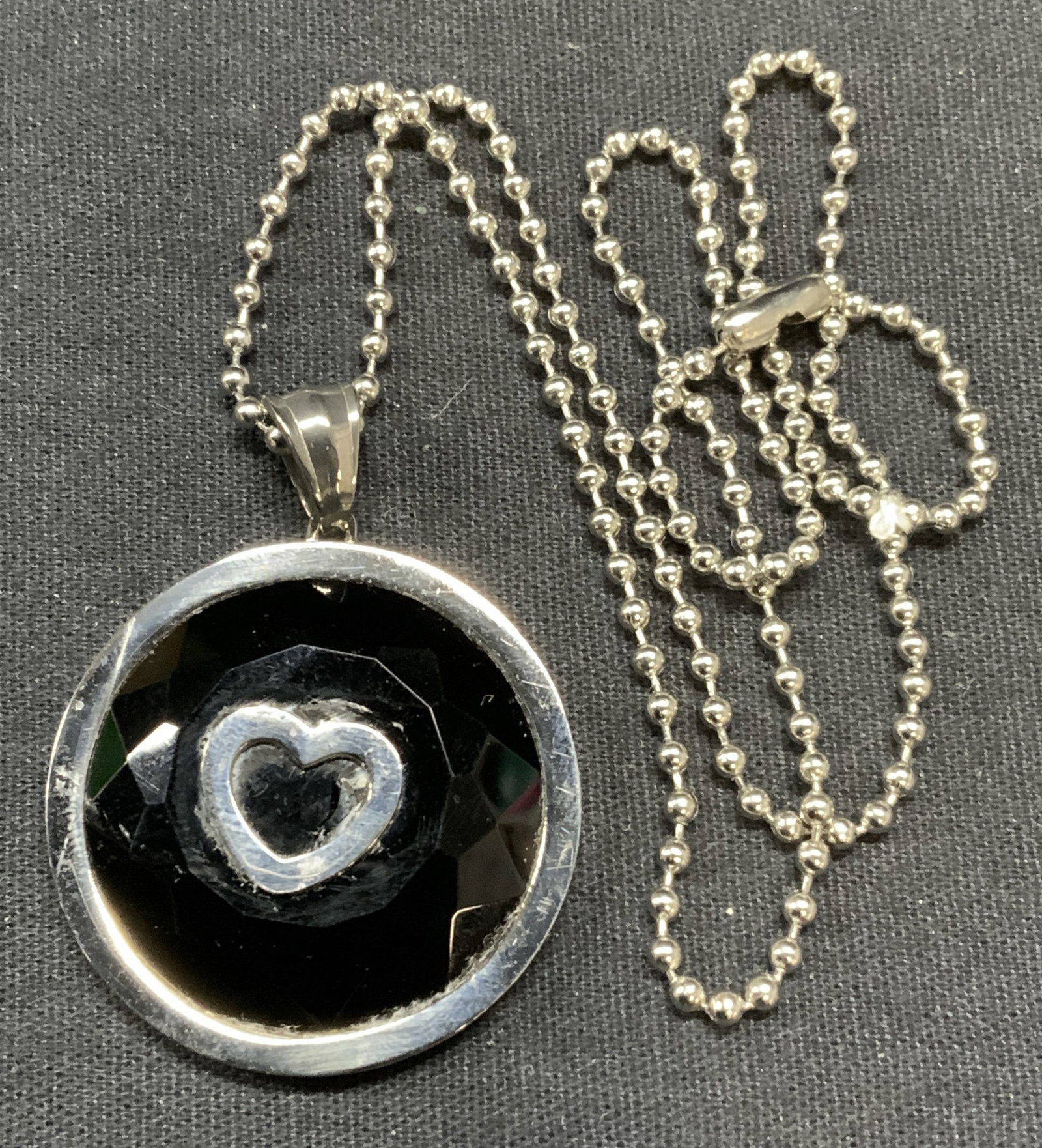 Stainless Steel Black Crystal Heart Necklace: Stainless steel pendant necklace with black crystal and heart decoration. Drop length approx. 9.5 inches, pendant measures approx. 1 3/8 inches diameter. Some scratching observed. Estate jewelry, cost