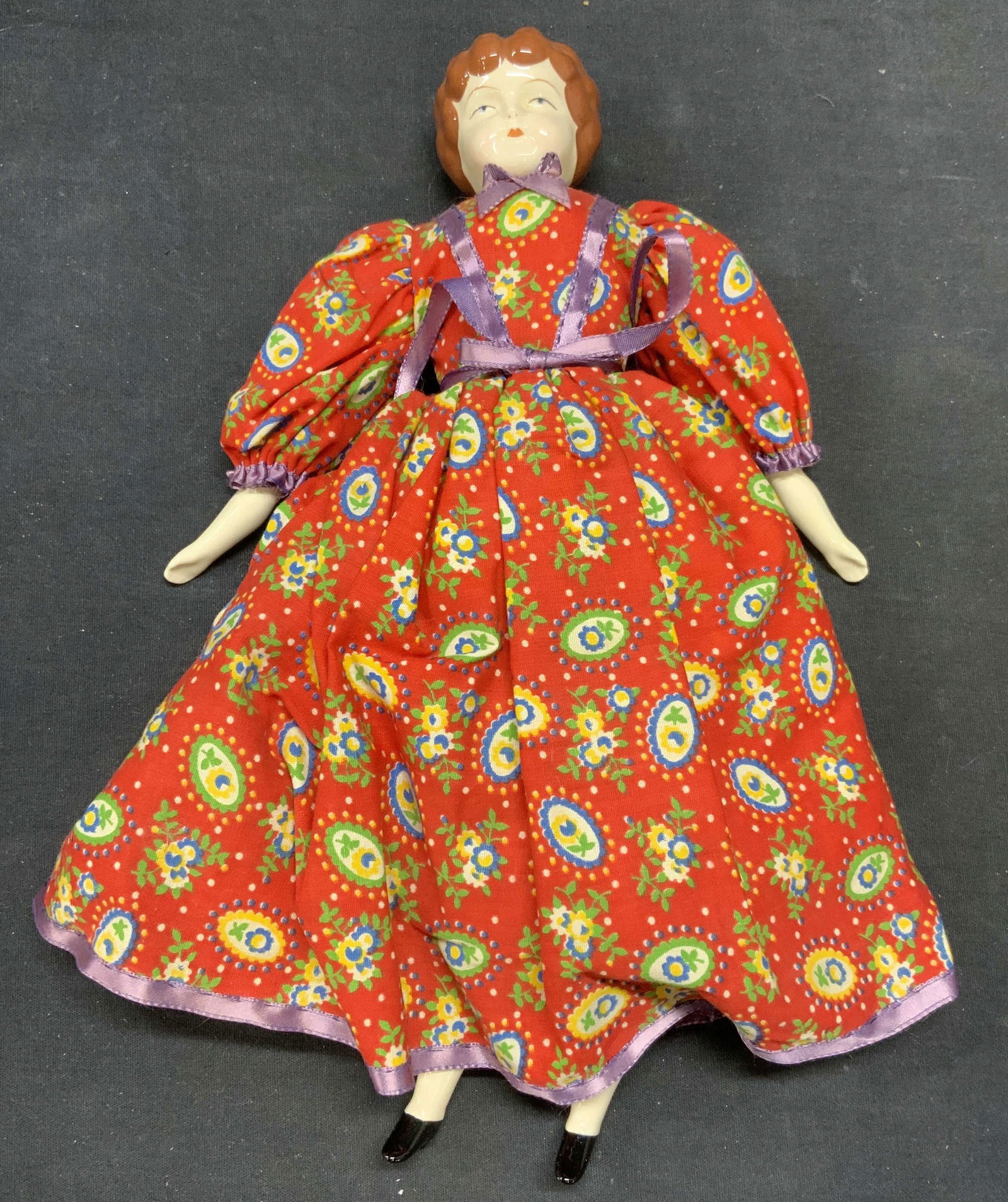Vintage Porcelain Doll with Red Dress: Vintage doll with porcelain head and limbs and fabric body. Red floral print dress. Measures approx. 12 inches long. Some wear to material and crazing observed. Doll, vintage doll, porcelain doll, fab