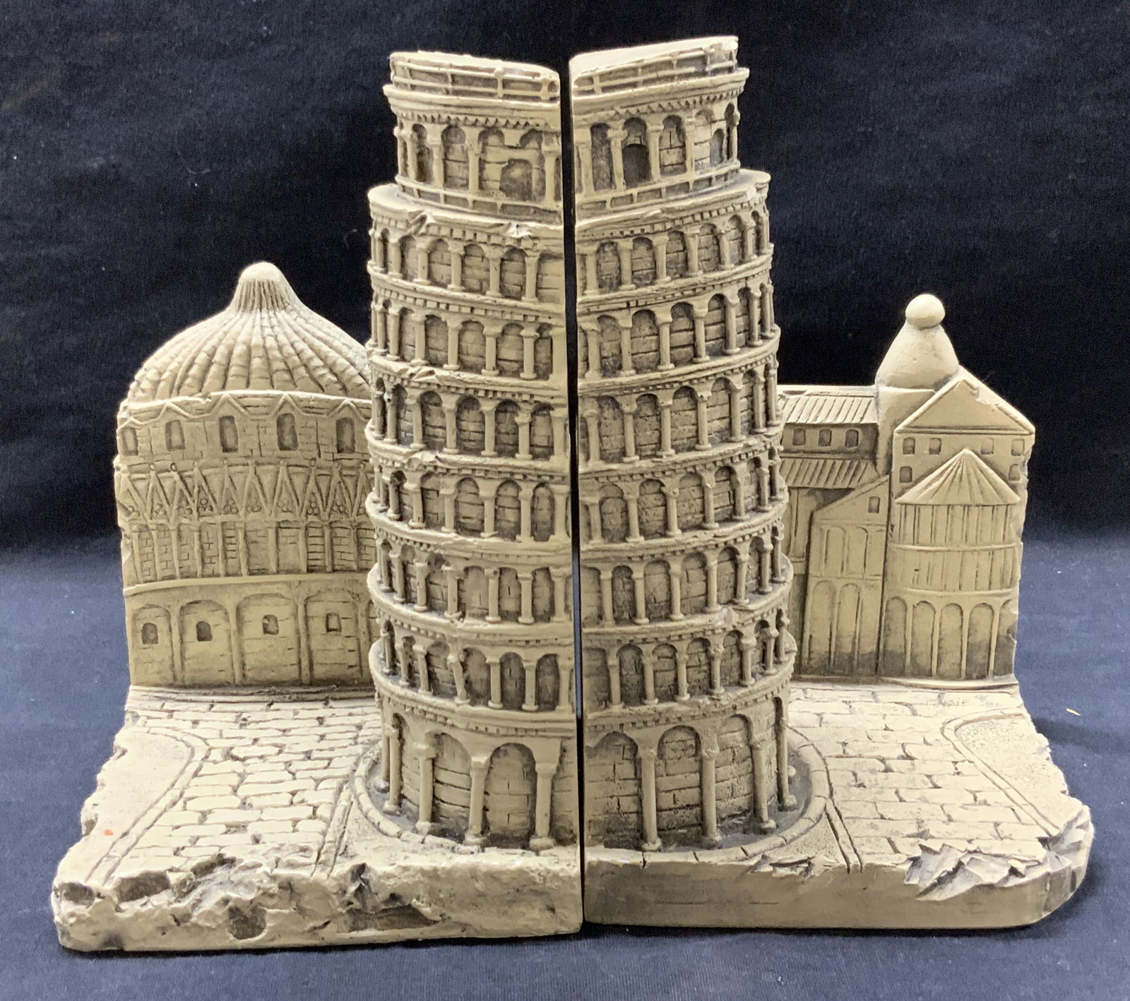 Pr TMS Hard Composite Tower Of Pisa Bookends: Pr of carved hard composite crafted bookends of the leaning tower of Pisa. Marked tms 2002 on backsides. Approx 7.25 inches tall and 9 inches long and 4 inches wide. Moderate wearing to bookends and b