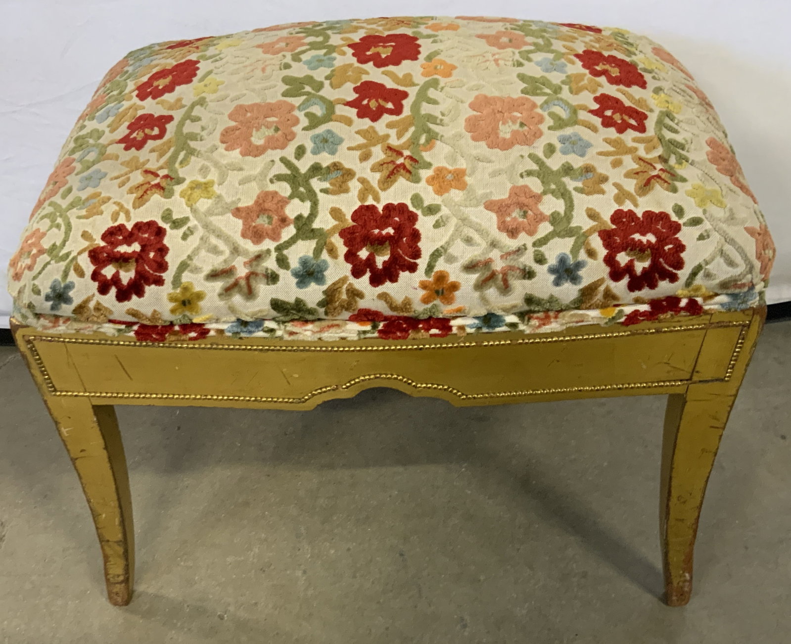 Vintage Floral Embroidered Gilt Wood Footrest: A vintage gilt wood frame stool with a multicolored floral embroidery top. Measures approx. 17H x 21W x 15D in. Tag to underside reads REMADE AND RENOVATED EVETTE Interiors. Some surface wear, discolo