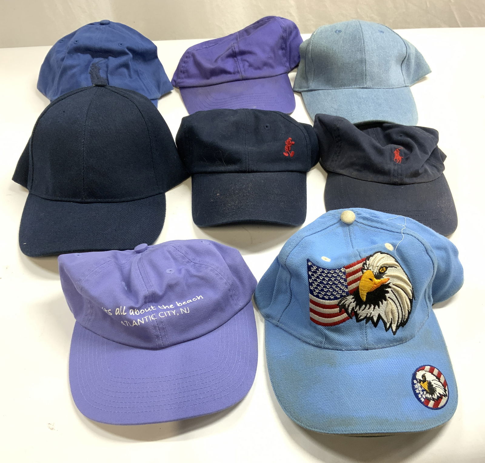 Lot 8 Baseball Caps, Polo Ralph Lauren & More: Lot includes 1 light blue with bald eagle and American flag, 1 denim hat, 1 navy hat, 1 purple hat, 1 navy with red toned Mickey Mouse logo, 1 navy with red toned Polo Ralph Lauren Logo, 1 purple whic
