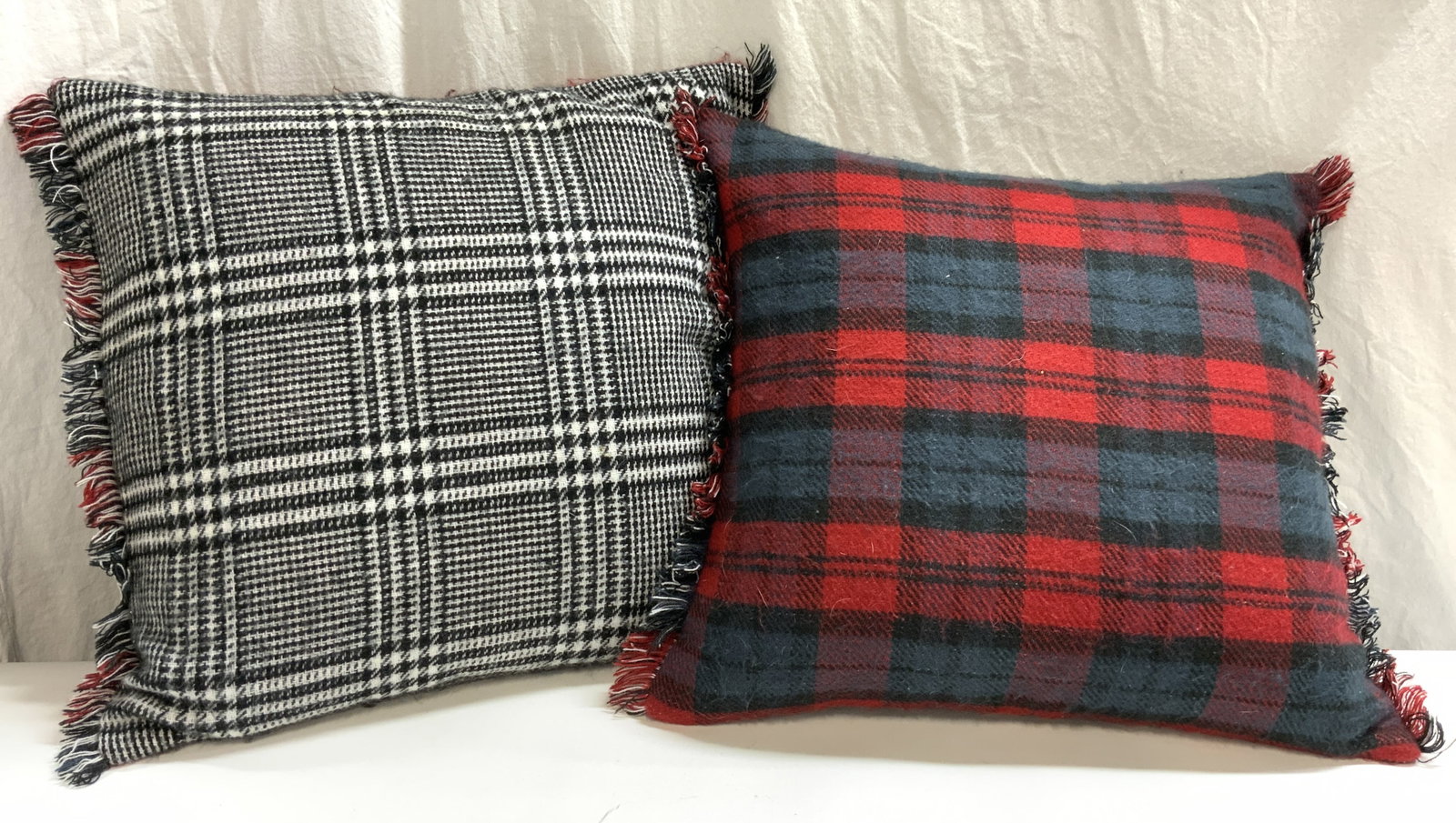 DIAMOND & BARATTA Pr Custom Cashmere Pillows: Lot includes 2 pillows. Each have plaid upholstery, red, navy & black to one side, black & white with areas of houndstooth detail to other side. Each pillow has fringes at side edges. Pillows each mea