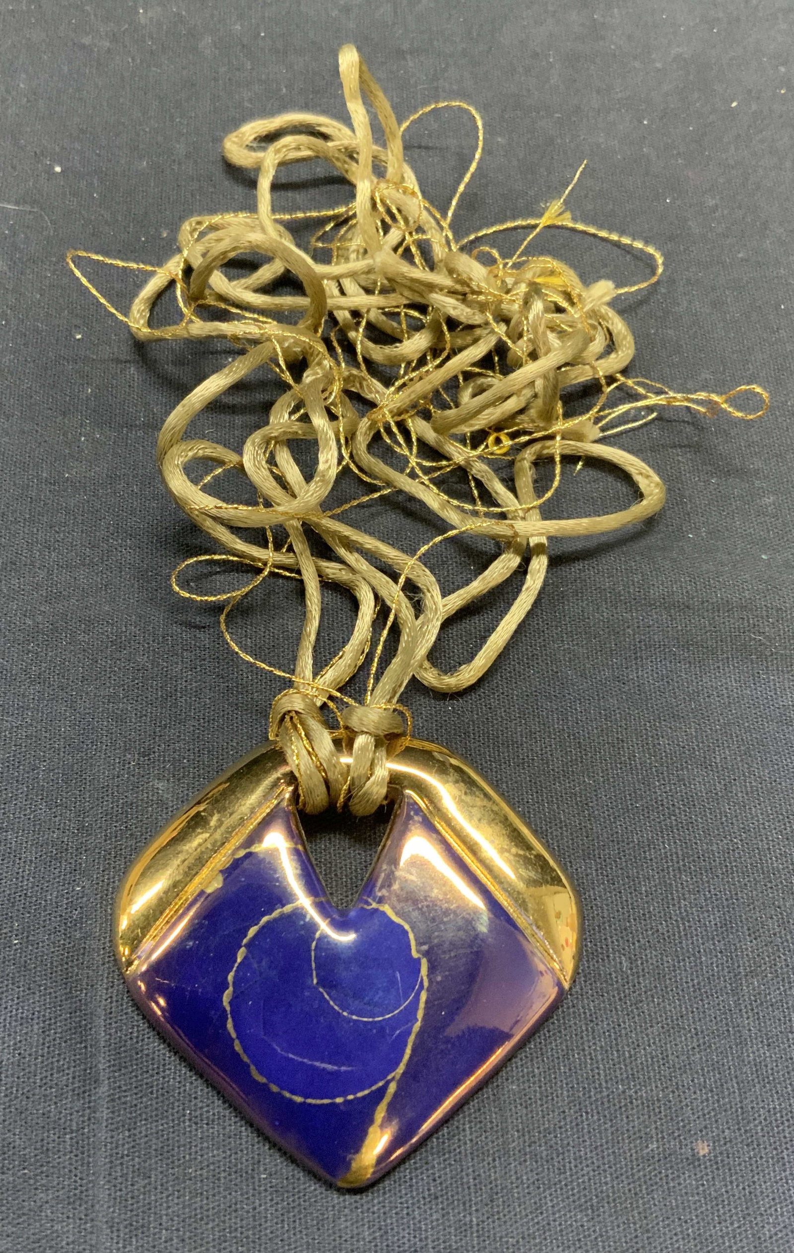Signed Gilt Ceramic Pendant Necklace: Signed ceramic pendant necklace with gilt and blue glazed pendant on gold tone cord. Signed illegibly to underside. Drop length approx. 14 inches. Pendant measures approx. 2 x 2.25 inches. Some scratc