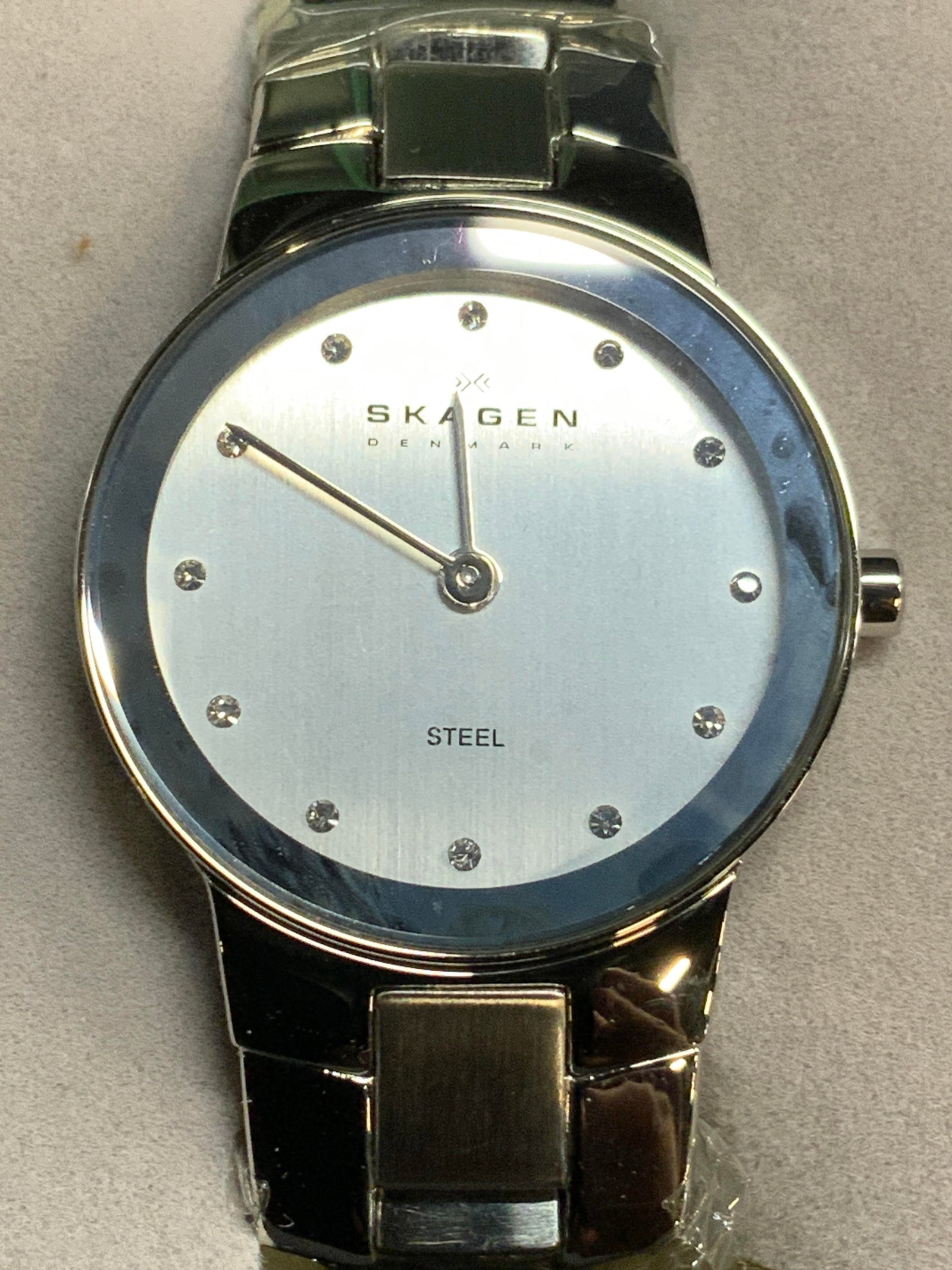 SKAGEN DENMARK Wristwatch W Orig Box: Watch face reads SKAGEN DENMARK. Piece is silver toned, with steel watch face as marked. Rhinestone detail & Deployment band. Lot includes original trademarked box with lid. Timepiece warranty card & 