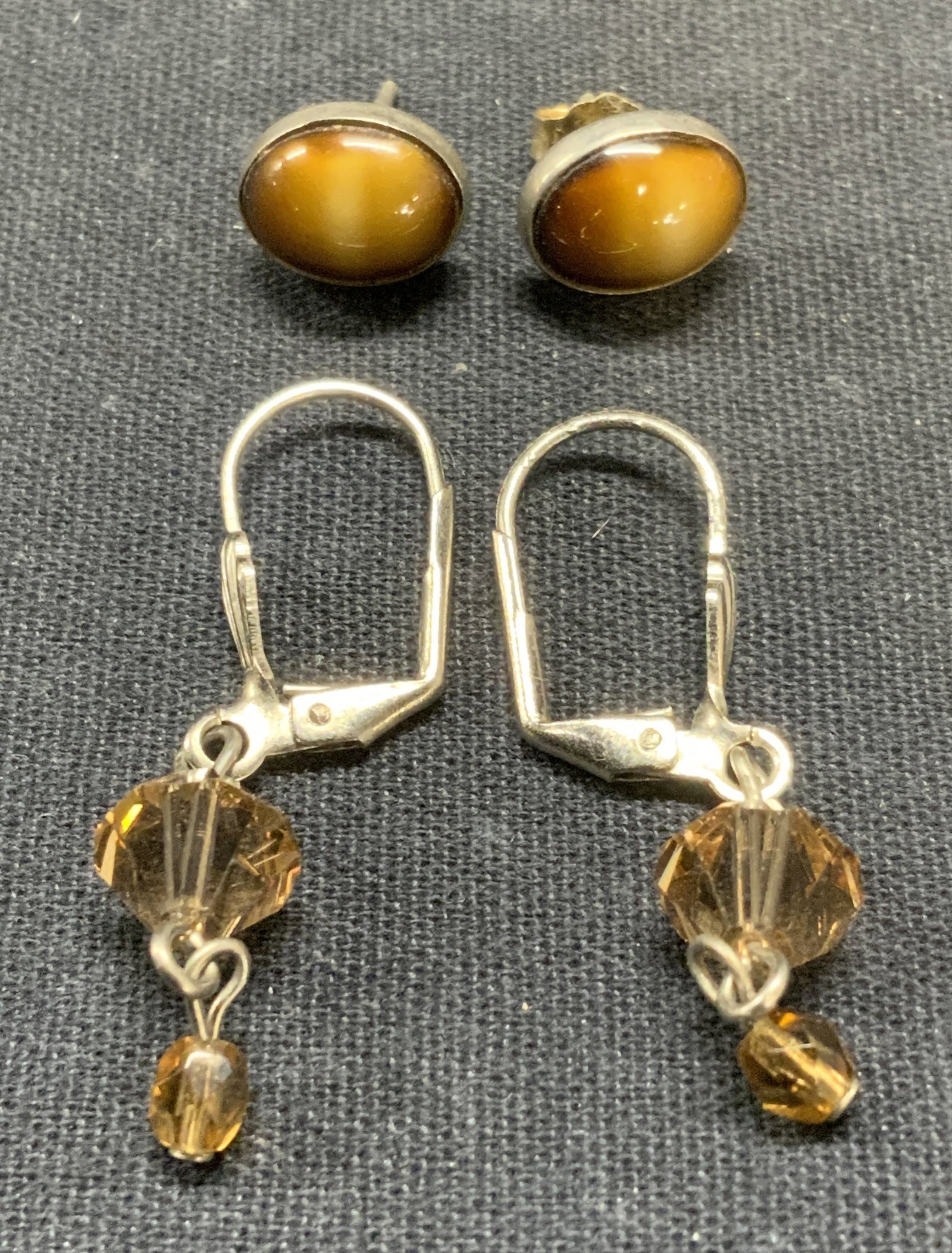 Lot 2 Silver Tn Crystal & More Earrings: Lot of 2 silver tone earrings. One pair with amber style crystal beads, hook backing. One pair with tigers eye style cabochon, post backing. Largest pair measure approx. 1 1/8 inches long. Some scratc