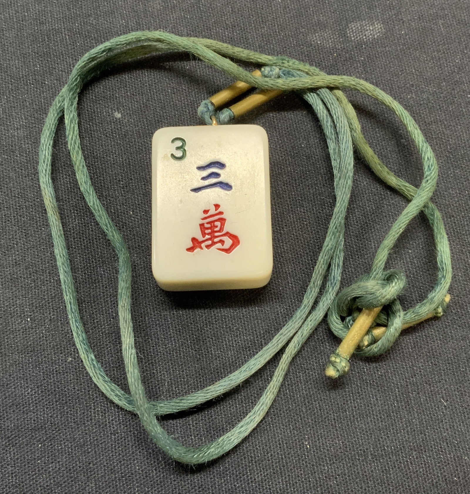 Vintage Mahjong Tile Pendant Necklace: Vintage necklace with mahjong tile pendant on green cord. Drop length approx. 12.5 inches. Mahjong tile approx. 1.25 x 1 inches. Some scratching observed. Estate jewelry, costume jewelry, cocktail jew