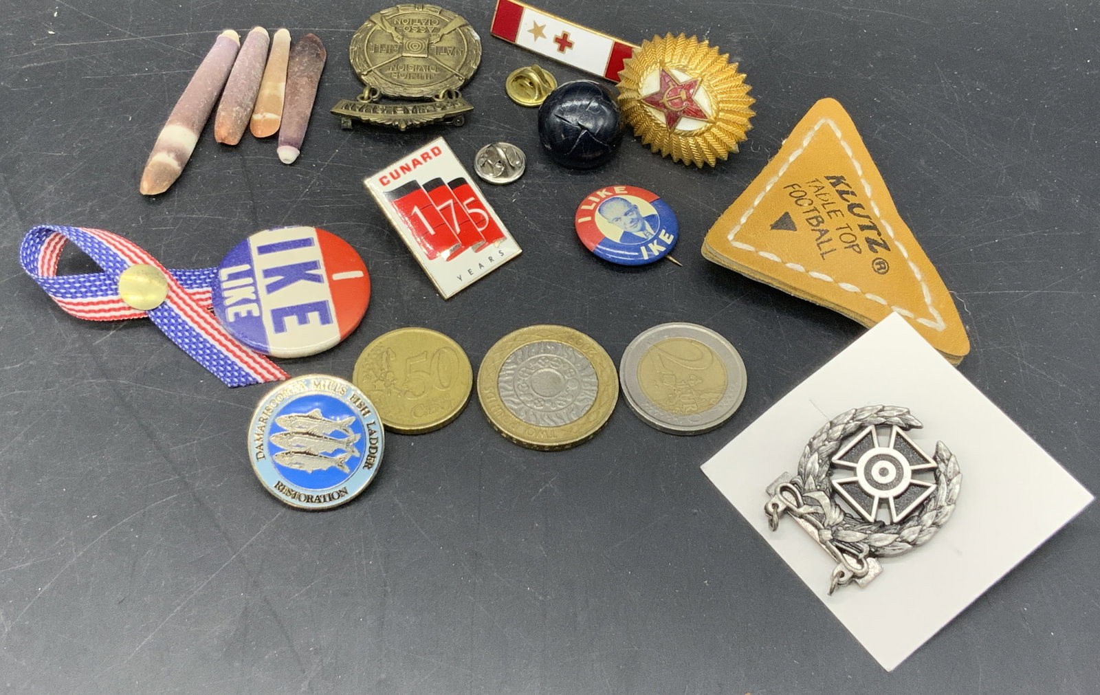 Lot 18 Buttons, Coins, Pins, Accessories & More: A group lot consisting of eighteen pieces. Lot includes coins, pins, a button, shells, and more. Pin motifs feature presidential, political, American, NRA, and more. Largest item is a Klutz Table Top 