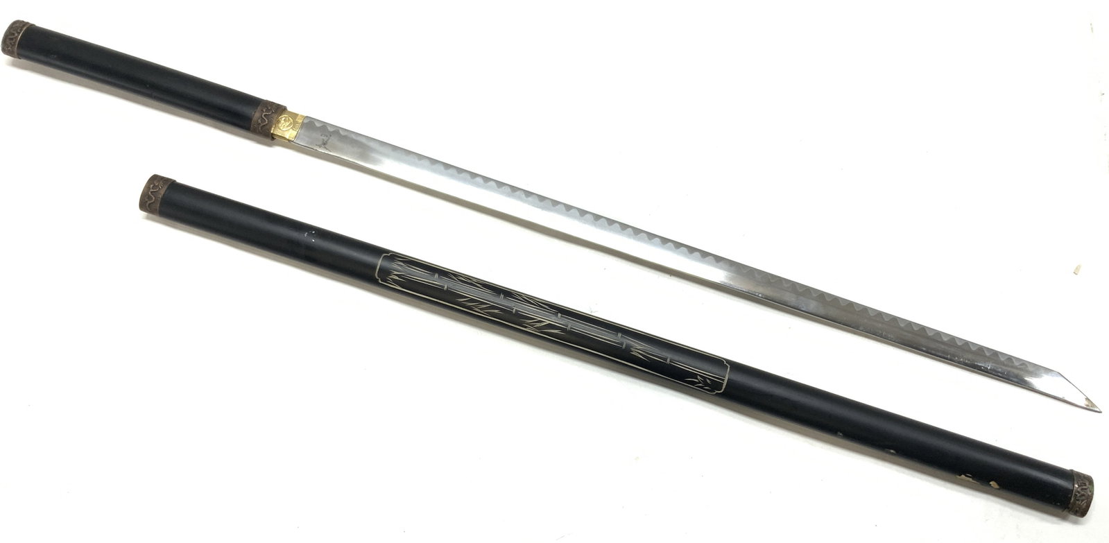 Steel Katana W Carved Wooden Sheath 3.5ft: Straight blade katana with carved wooden sheathe with bamboo motifs and bronze toned caps on ends of sheath and handle with. Marked in blade BLP with a figure motifs on edge of blade. Blade does not a