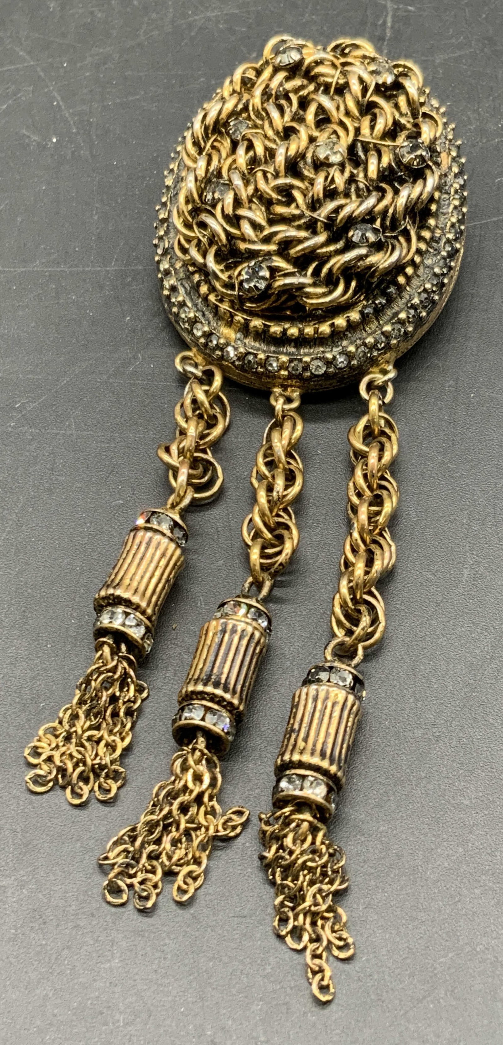 VOGUE JLRY Vintage Dangling Tassel Pendant Brooch: A multihued gold tone metal brooch featuring dangling chain tassels and faceted crystals. Raised metalwork details throughout. Reverse features a pin closure and a bail. Signed VOGUE JLRY to reverse. 