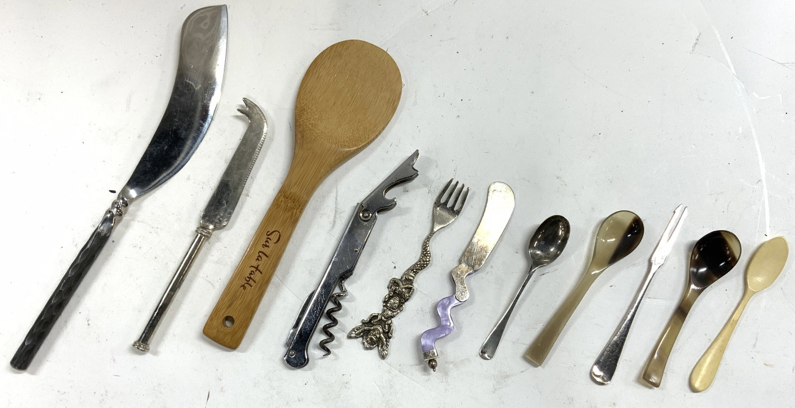 Lot 11 Kitchenware Utensils Sur La Table +: Lot includes 1 wooden spoon trademarked SUR LA TABLE, 1 bottle opener corkscrew, 1 cheese knife w purple handle, 1 hors Doeuvres fork, 1 hors Doeuvres fork with mermaid handle, 1 butter knife, 1 carve