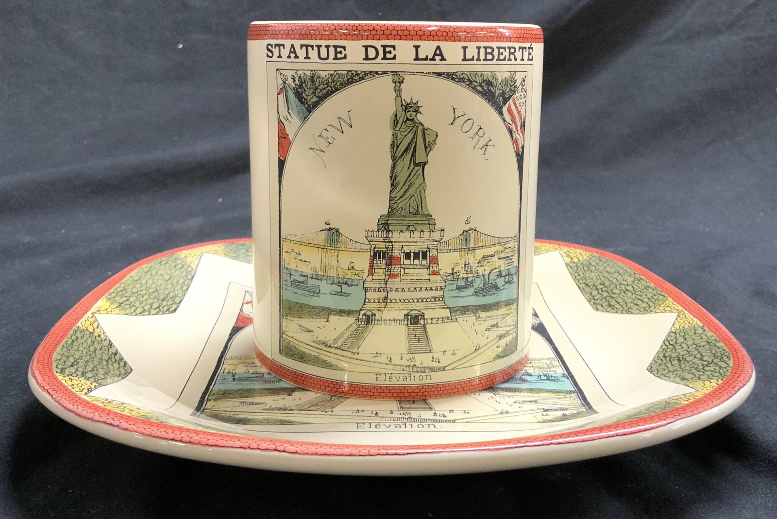 MMA Coffee Cup & Plate PORTUGAL: Each piece marked MMA MADE IN PORTUGAL on underside. Lot includes 1 cup & 1 Plate. Each are porcelain. Each have depictions of The Statue Of Liberty. Orange toned detail at edges. Plate measures appro