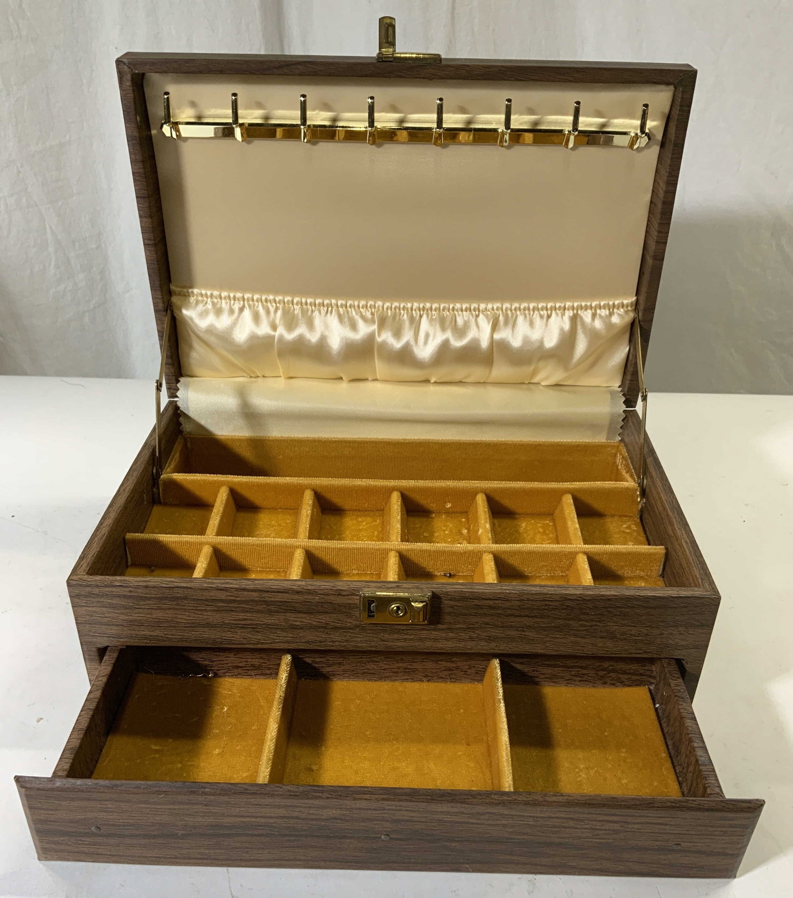 MELE Vintage Wood Style Lidded Jewelry Box: Locking mechanism reads MELE. Jewelry box is brown toned with wood style. Piece has hinged lid. Interior has goldenrod & cream toned lined interior. Lower tier slides out simultaneously with opening l