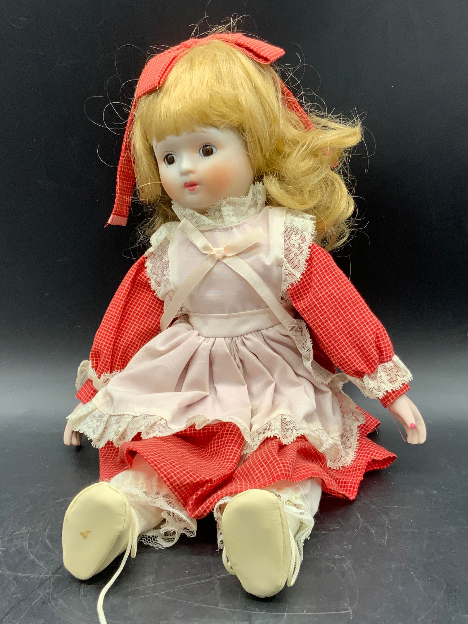 Vintage Porcelain Limb Doll W/ Dress: A vintage doll wearing a red and white fabric dress. Doll has porcelain limbs and a fabric body. Measures approx. 16L x 5.5W in. Some discoloration and surface wear present. Collectibles, vintage doll