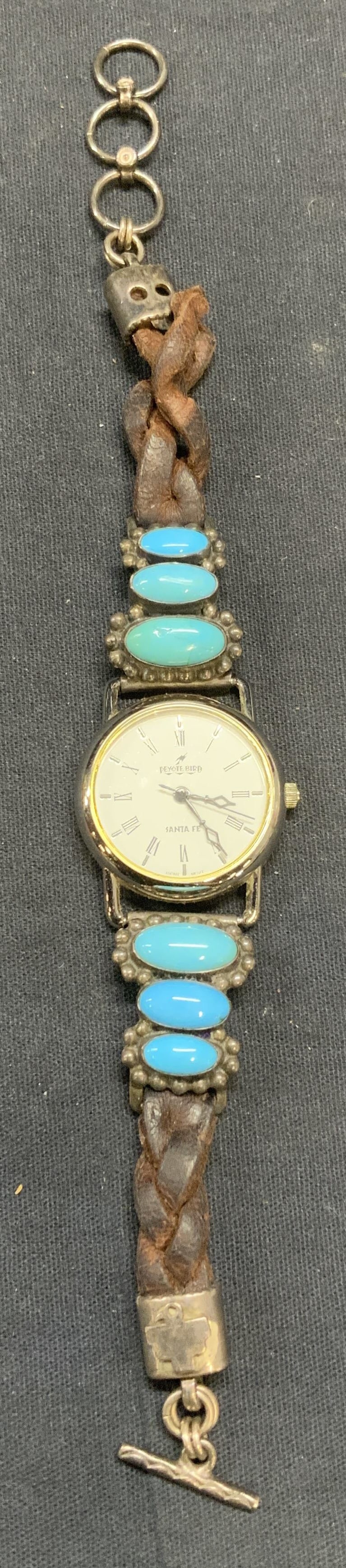 Peyote Bird Sterling Silver Leather Watch: Watch Peyote Bird watch with brown braided leather strap and turquoise stones. Sterling silver accent on strap, marked Feeney for Don Lucas. Signed on face. Measures approx. 7.5 inches long. Face appr