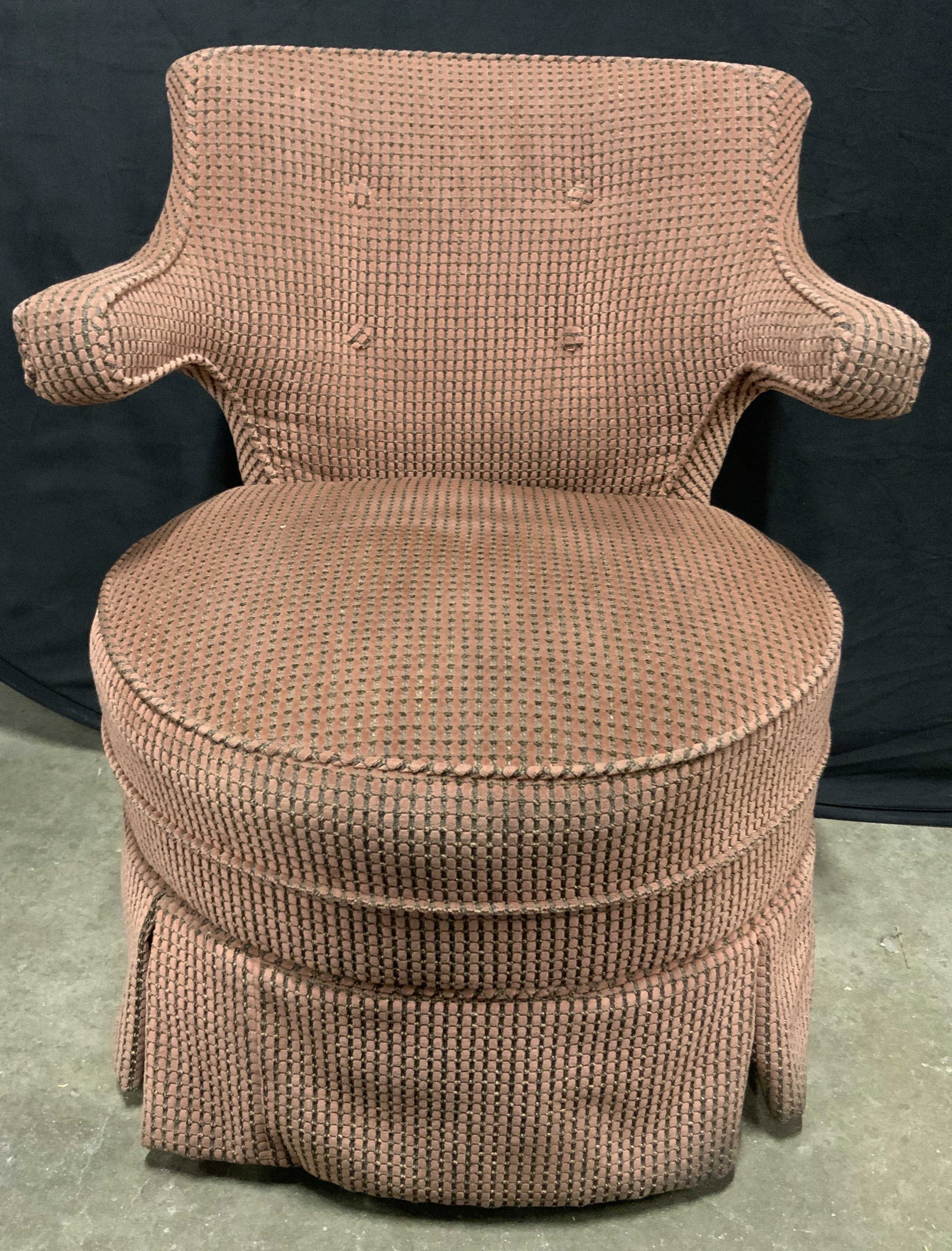 Vintage Upholstered Swivel Armchair: A vintage upholstered swivel armchair. Upholstered in a soft hand material. Unique raised arms. Skirted base. Four wooden legs to base. Swivel mechanism to interior. Piece is weighty. Measures approx.