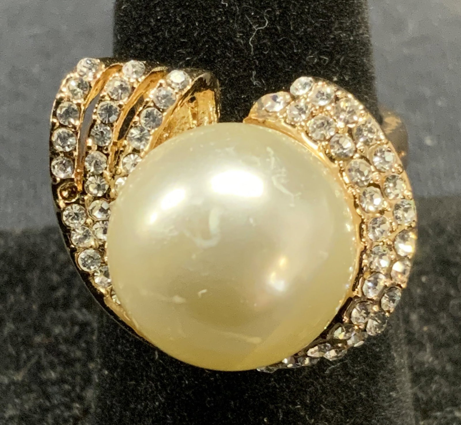 Gold Tone Faux Pearl Crystal Cocktail Ring: Gold tone cocktail ring with faux pearl and pave crystal setting. Ring size 7.5. Setting measures approx. 7/8 inches wide. Some scratching observed, one crystal needs replacement. Estate jewelry, cost