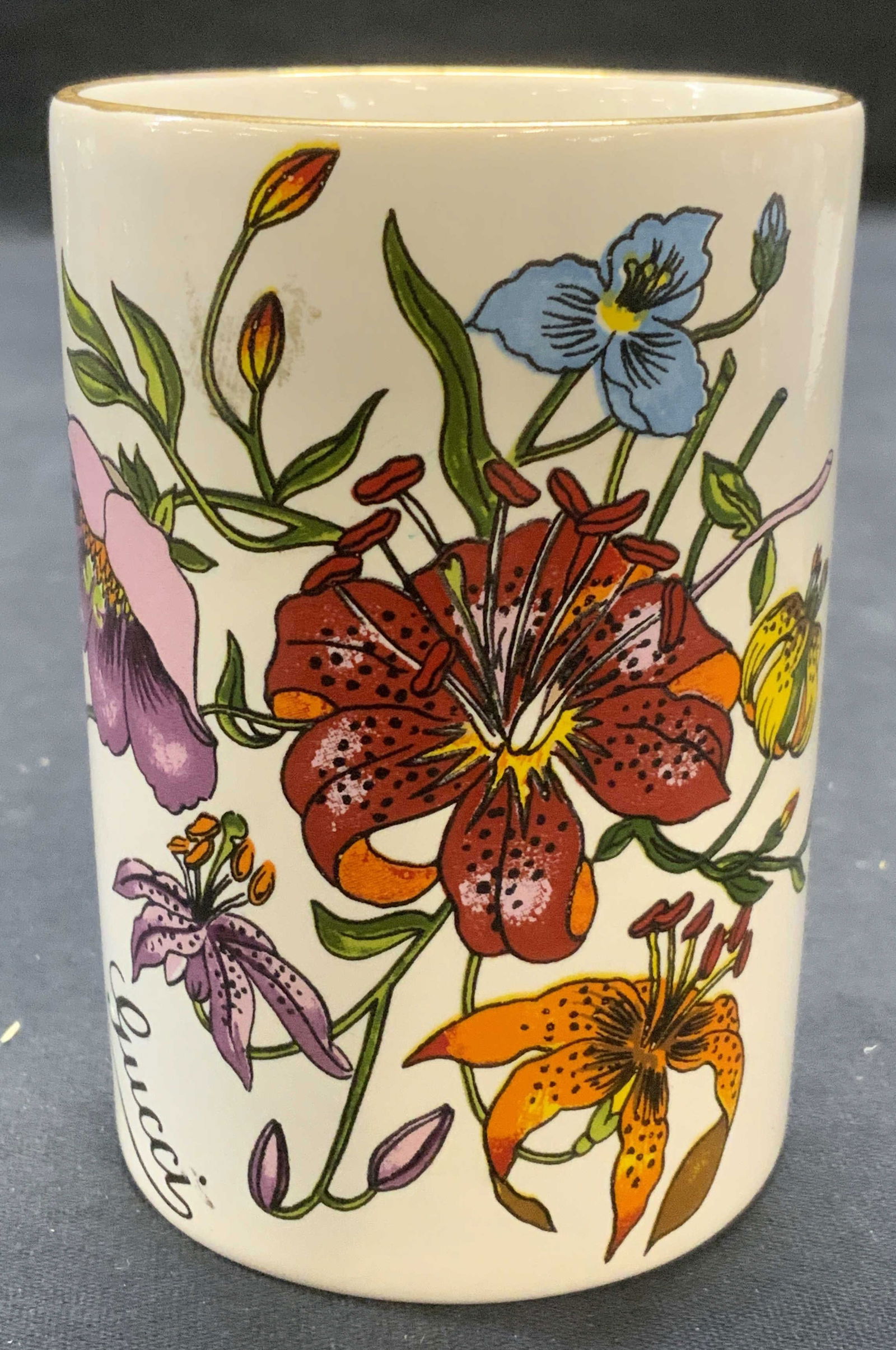 Gucci Gilt Floral Porcelain Vessel, Italy: Gucci porcelain vessel. Gilt rim and floral motif on body. Trademarked to underside. Made in Italy. Measures approx. 2.5 x 3 5/8 inches. Some surface wear including scratching observed. Gucci, Gucci v