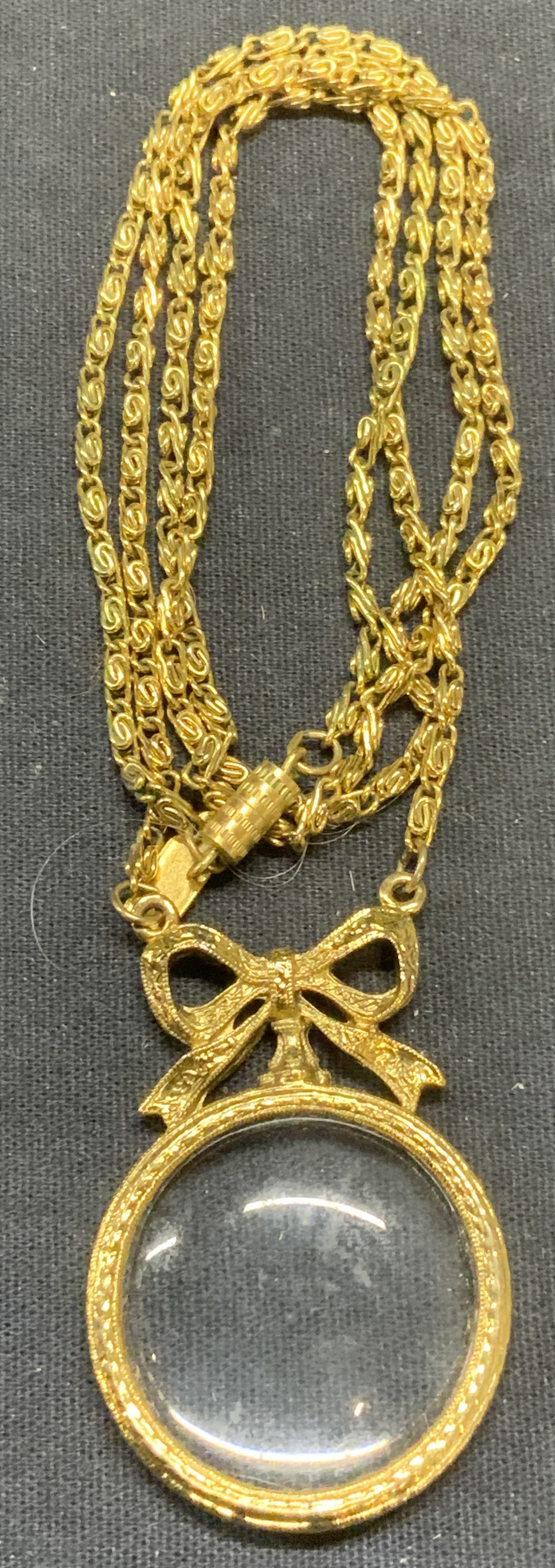 Sgn 1928 Gold Tn Magnifying Glass Necklace: Signed 1928 gold tone pendant necklace with magnifying glass pendant. Signed on hang tag. Drop length approx. 13.75 inches. Pendant measures approx. 2 x 1.25 inches. Some scratching observed. Estate j