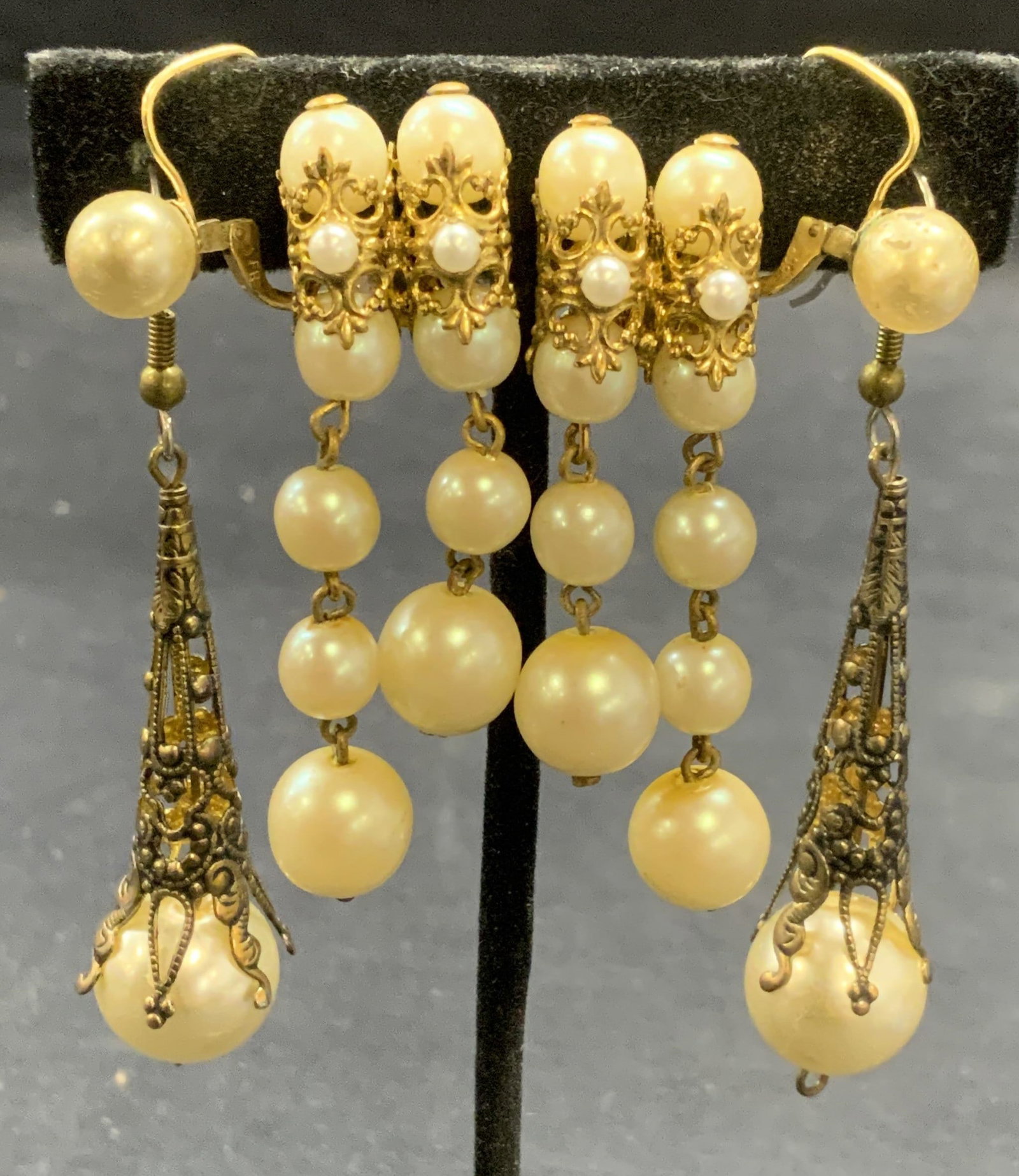 Lot 3 Gold Tone Faux Pearl Earrings: Lot of 3 jewelry pieces. Gold tone filigree and dangle faux pearl decorated earrings. 2 with hook backing, 1 with clip on backing. Longest pair measure approx. 2 inches. All pieces have some surface w