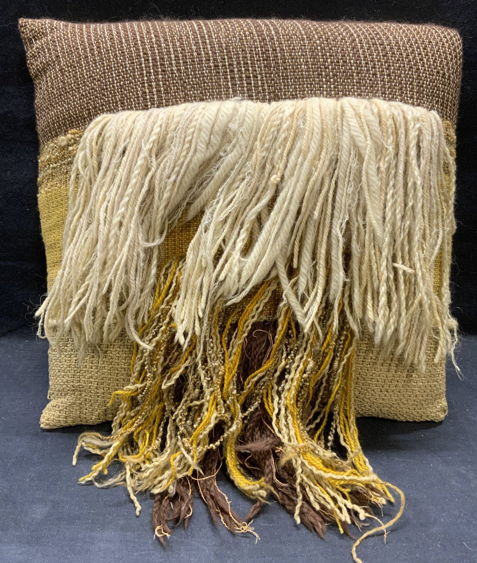 Tan, Yellow, Brown Woven Fringe Pillow: Tan, yellow, and brown toned woven pillow with yarn fringe. Material feels like natural fiber. Measures approx. 15.5 x 14.5 inches. Some wear to material including pulling observed. Pillow, accent pil