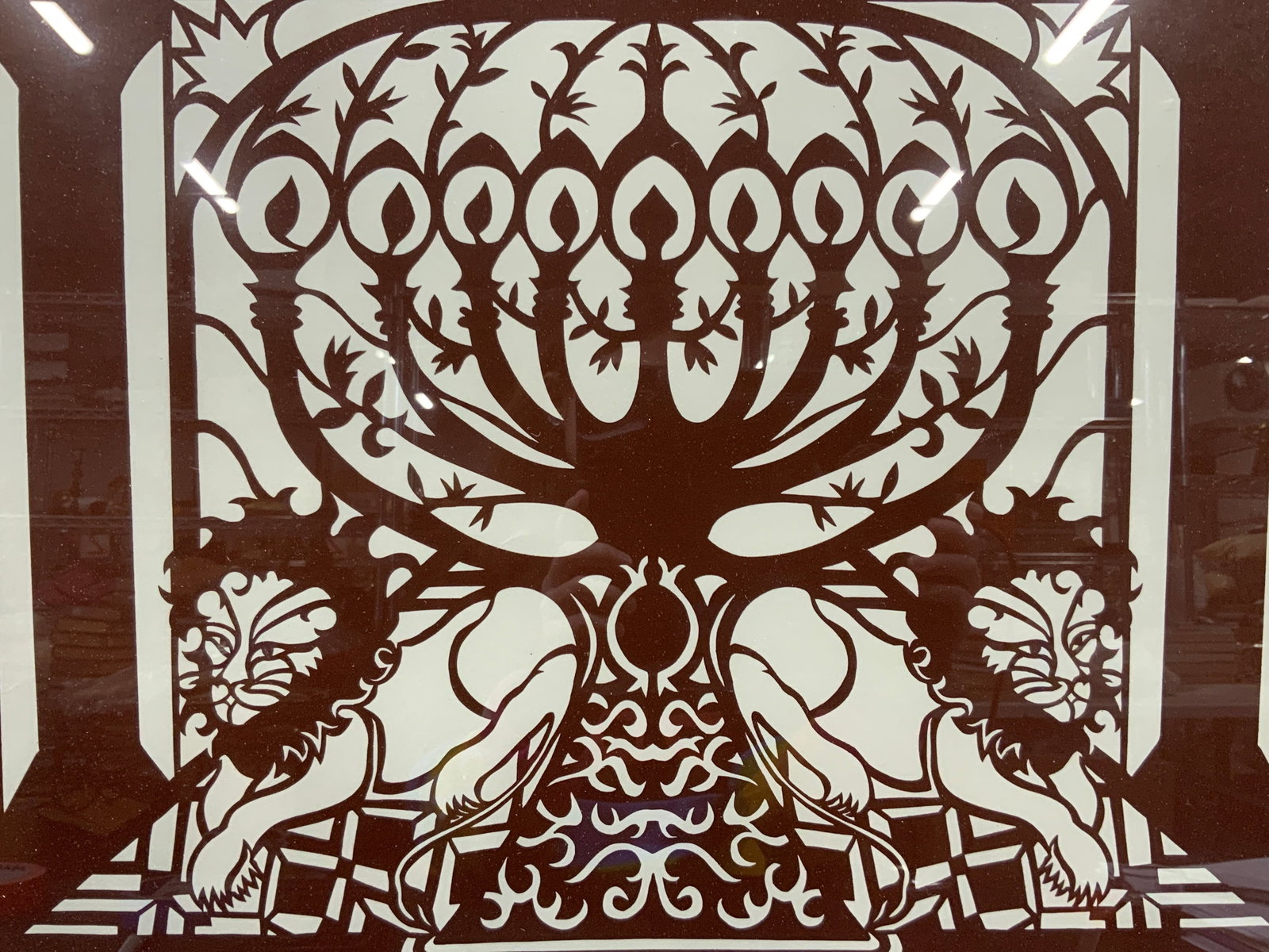 Judith Hanloin Sgd Judaica Paper Cut Out: A paper cut out depicting a red toned Menorah flanked by lions. Signed Judith Hanloin, 1989, menorah, 16/203 Framed in a red toned wooden frame . Approx 22.5 x 28.5 inches, window measures 15 x 20 inc
