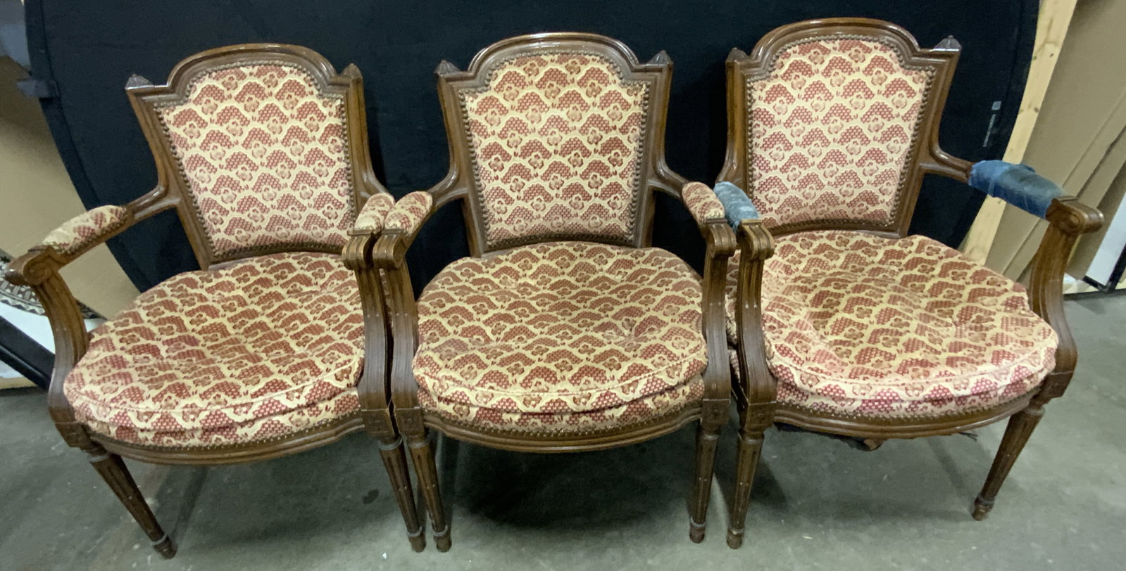 3 Antique French Louis XVI Upholstered Armchairs: Antique, possibly vintage, French Louis XVI style upholstered armchairs. Carved woodwork throughout, scrolled arms. Upholstery is a soft hand patterned red & neutral hue. Nailhead accents. Measures ap