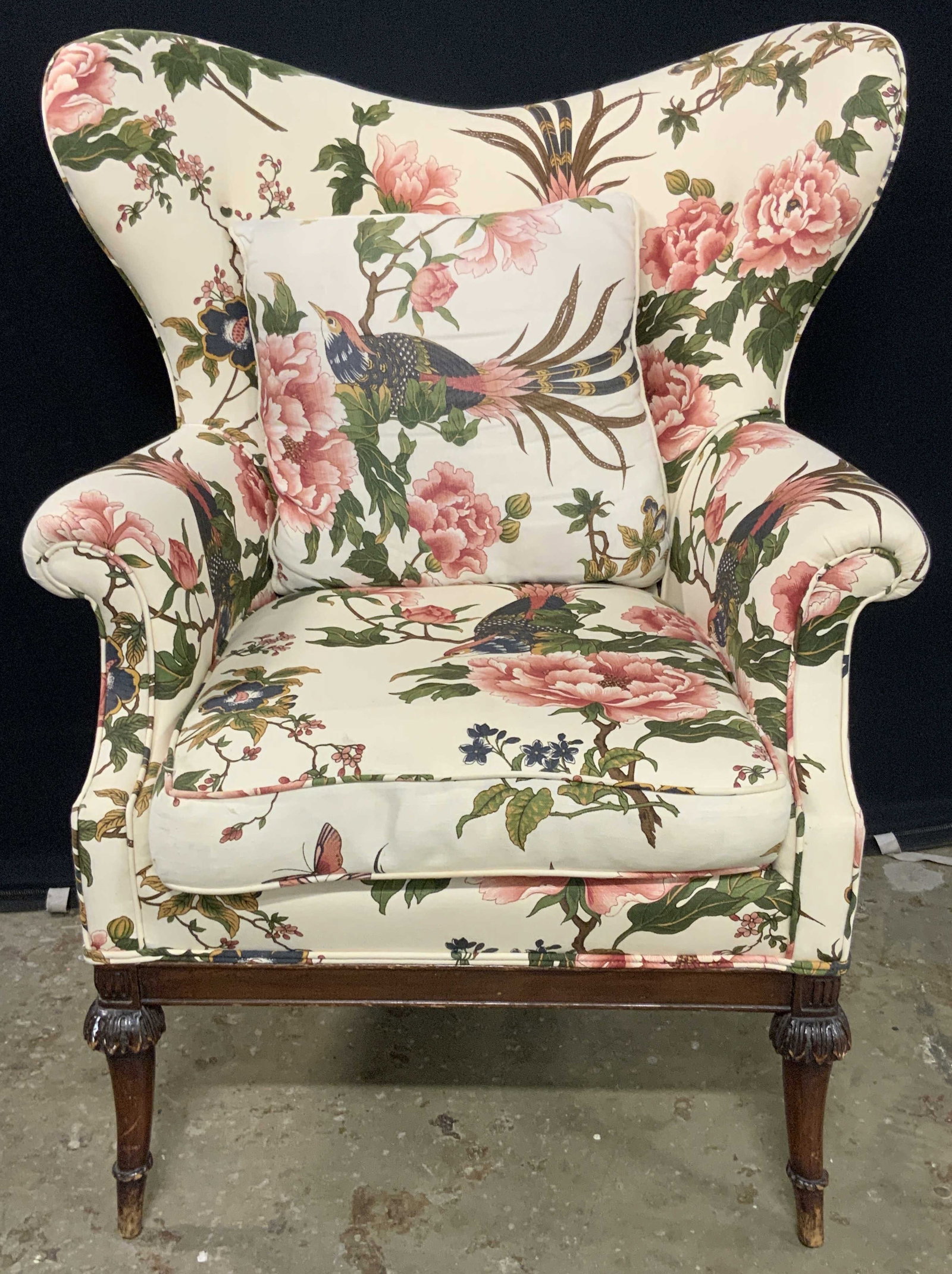 Vintage Butterfly Wing Back Upholstered Armchair: A vintage butterfly wing back armchair featuring a colorful bird & floral motif upholstery. Cream toned with pops of blue, green, pink, and brown hues throughout. Carved wooden front legs. Chair measu