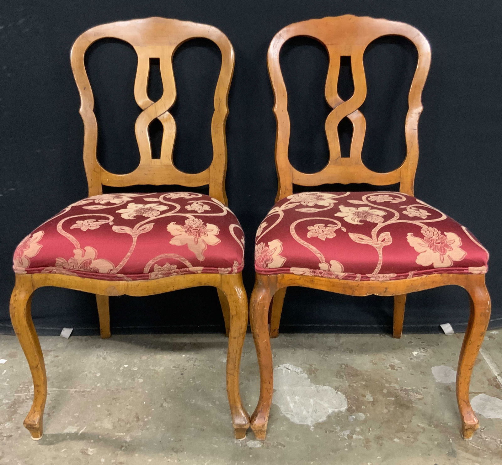 Pair Vintage Carved Wood Floral Upholstery Chairs: A pair of vintage chairs featuring carved wood frames and upholstered seats. The frames feature curved front legs and open backs. The seats are upholstered in a red soft hand fabric decorated with a f
