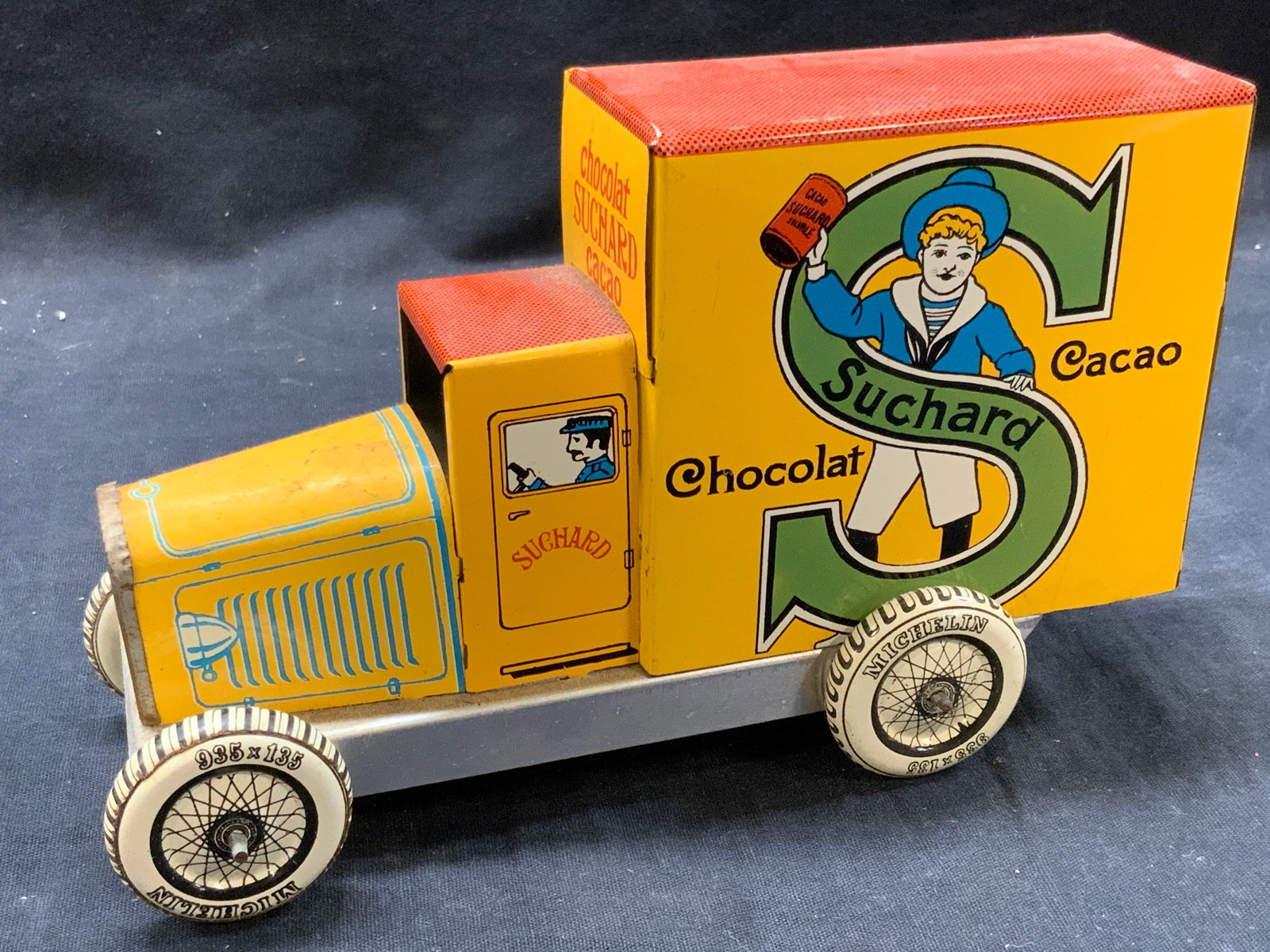 Vtg Suchard Chocolate Aluminum Truck Toy. France: Vintage aluminum or tiny made toy truck. Marked France. Toy truck with moveable wheels with a decal of a boy within an S reading Suchard Chocolat Cacao. Approx 5 inches tall and 7,5 inches long. Moder