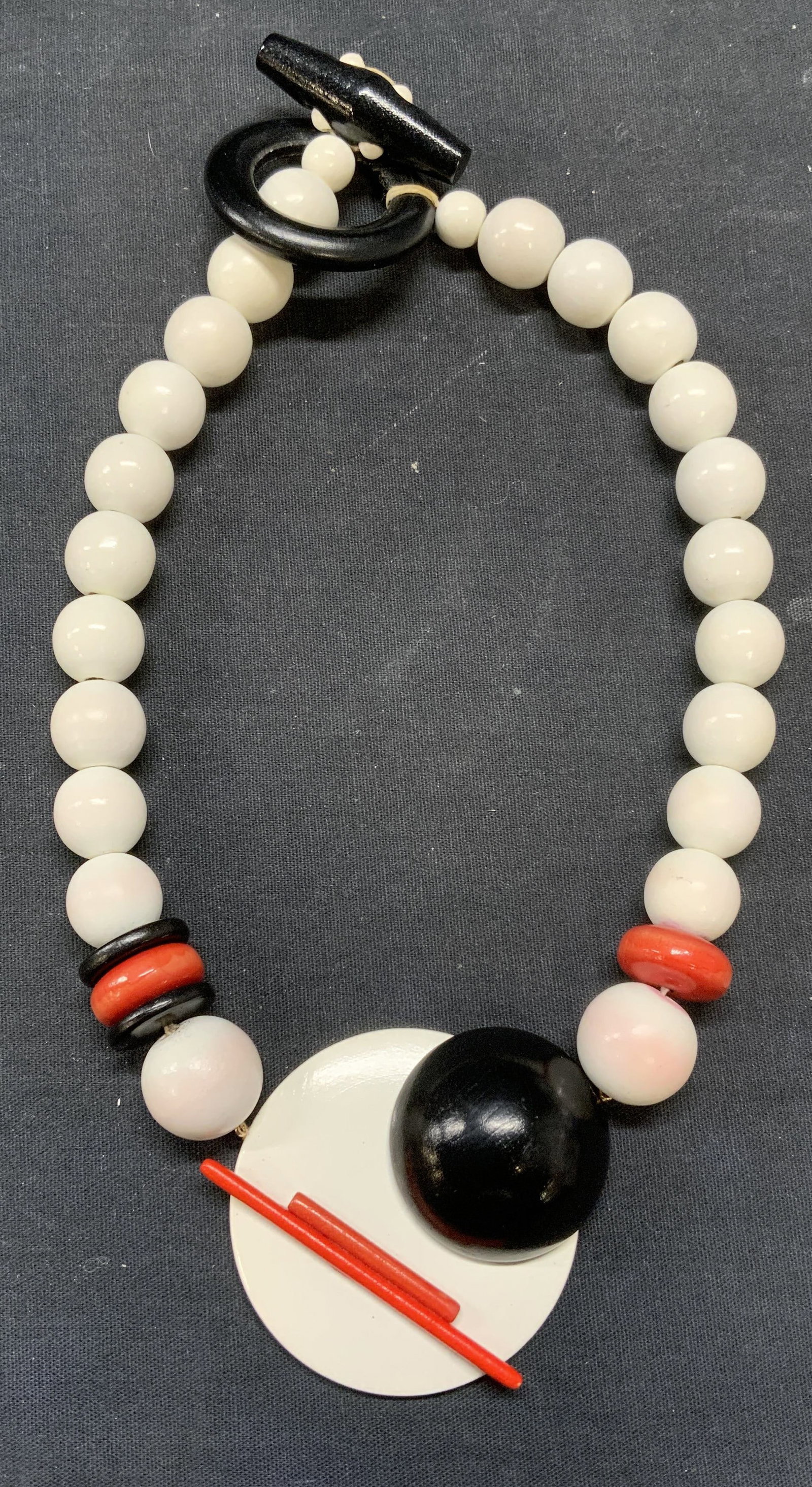 Vintage Wood Beaded Pendant Necklace: Vintage wood beaded pendant necklace with geometric motif in black, white, and red. Drop length approx. 7 inches. Pendant approx. 2.5 inches wide. Some surface wear including scratching observed. Esta