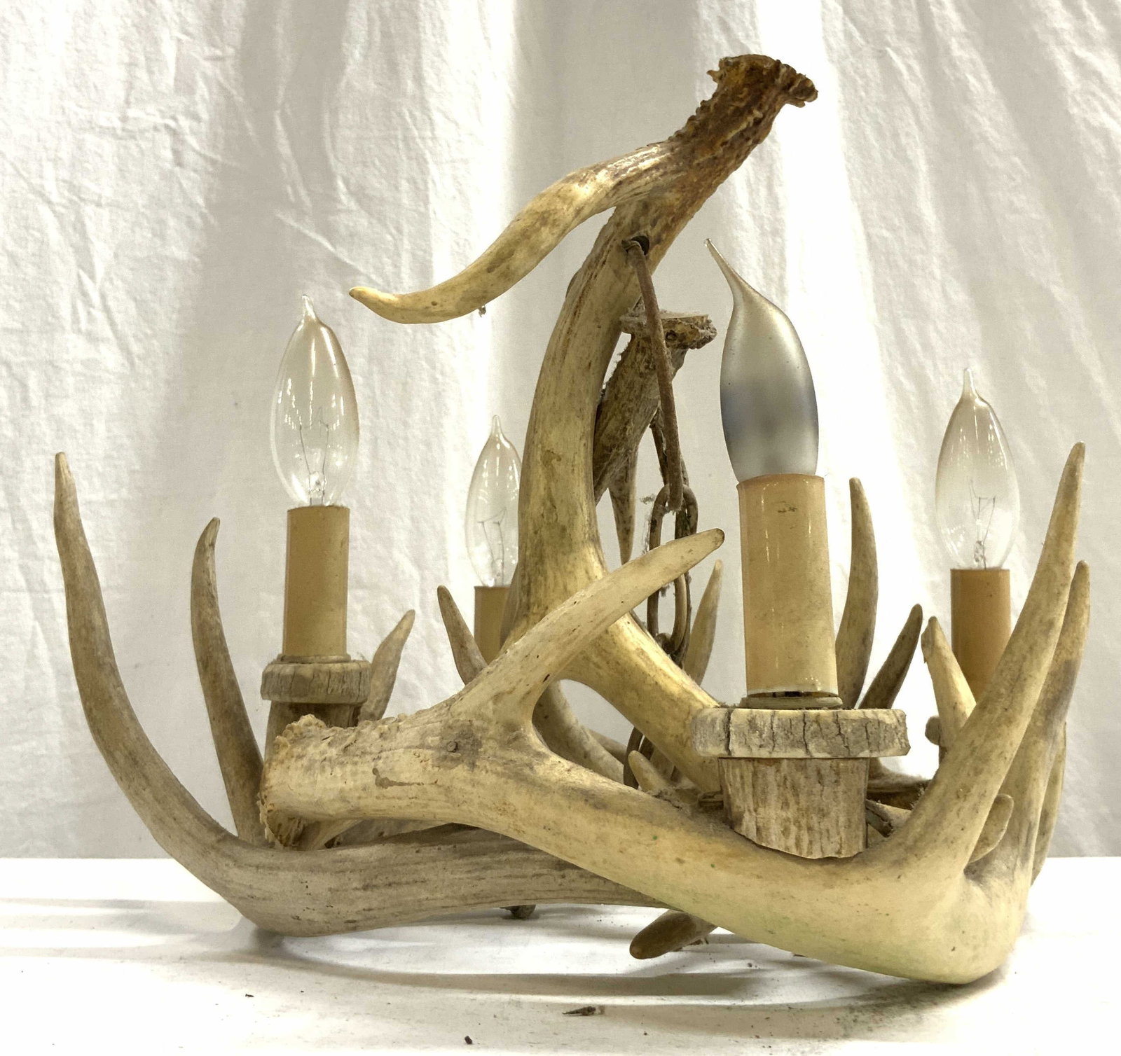 Vintage Four Arm Antler Chandelier: Chandelier appears to be vintage. Piece has 4 arms with bulb sockets. Chandelier appears to be crafted from deer antlers. Piece has small chain link at top. Piece measures approximately 15 inches wide