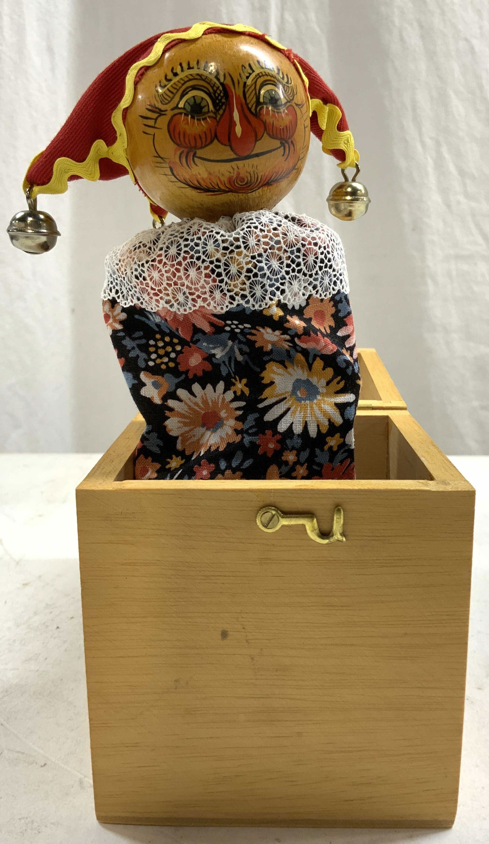 Vintage Wooden Jack In The Box W Lid: Jack in the box has tan toned wooden exterior with lid. Piece has cloth over spring with hand painted wooden head & jingle bell hat. Piece measures app 4 inches cubed when closed 7.5 inches tall when