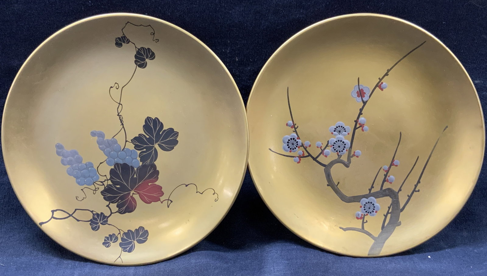 Set 2 Asian Lacquered Wooden Plates: Set of 2 gold toned lacquered wooden plates with Asian designs of a cherry blossom tree and grape vines on centers of dishes, Approx 7 inch diameter. Moderate wearing to center designs. Lacquered dish