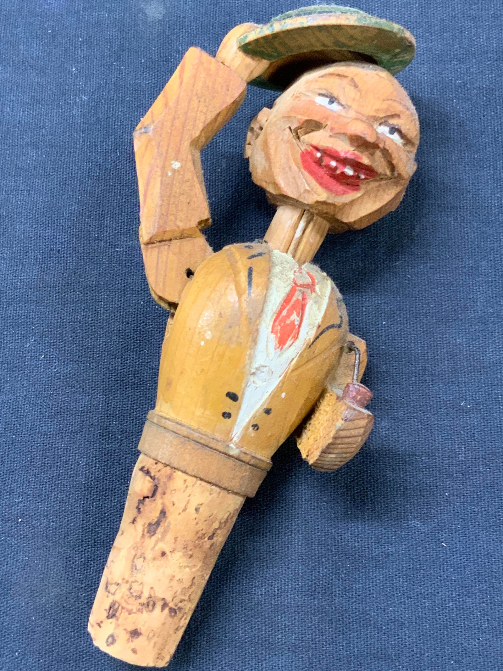 Vtg Carved Wooden Articulated Bottle Stopper: Vintage carved wooden bottle stopper with articulated moving puppet topper of a man holding a hat off his head, hand carved and hand painted. Approx 5.25 inches tall and 2 inches wide. Moderate wearin
