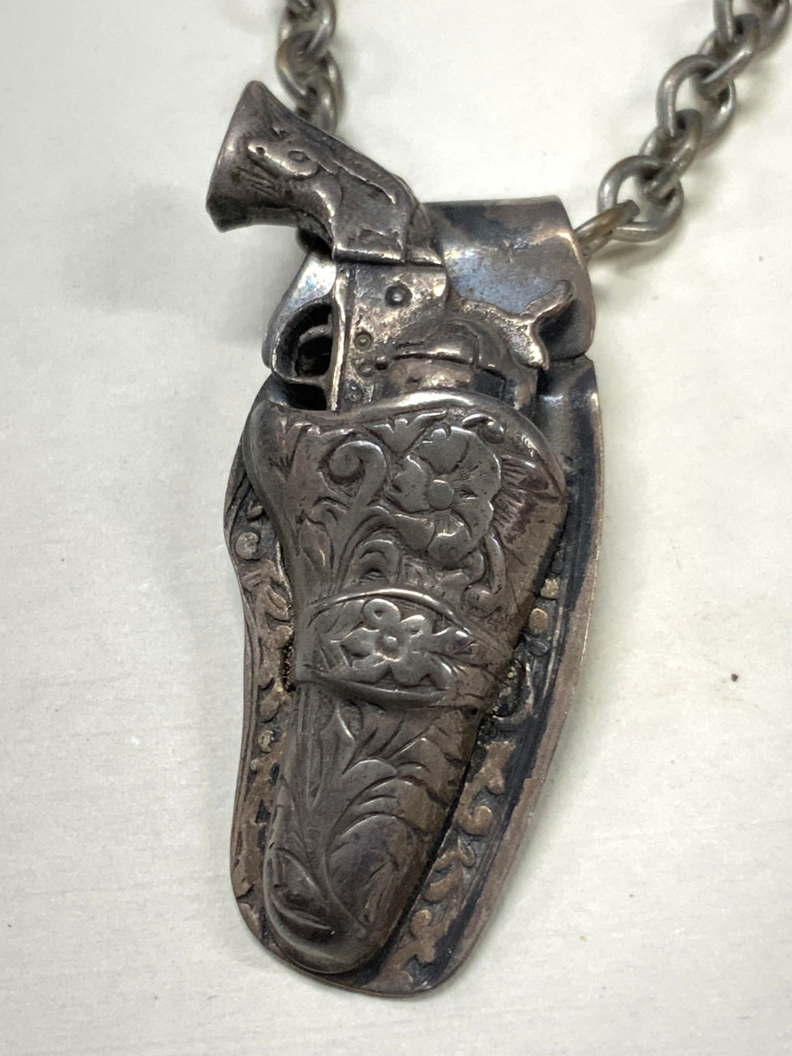 Vtg Sterling Silver Revolver Gun Tie Clip: Vintage tie clip with a sterling silver revolver charm affixed to a chain hanging from the clip. High detailing in the gun case and gun. Marked Sterling on gun. Approx 4.5 inches long and 2.25 inches