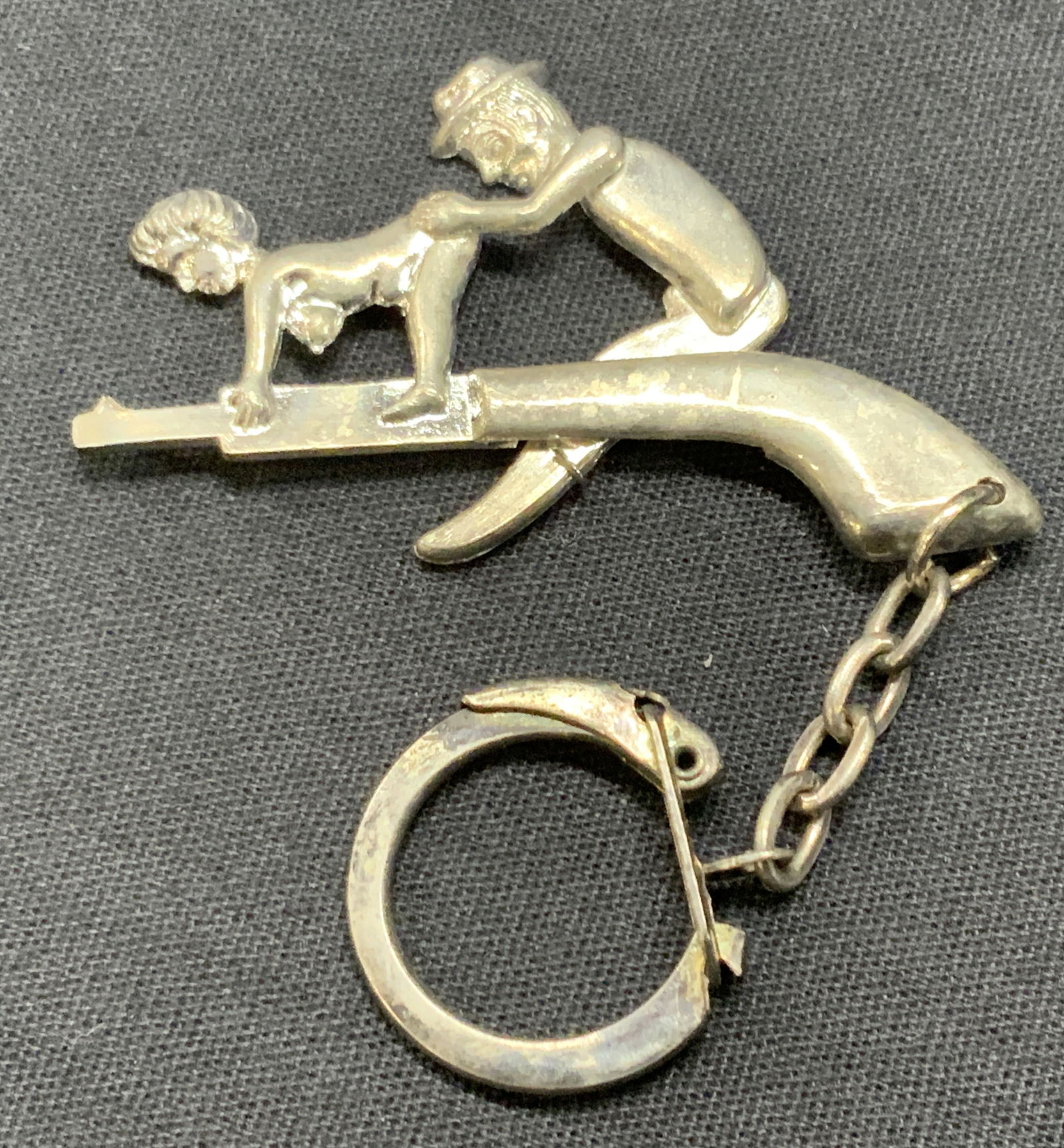 Vtg Metal Work Erotica Keychain: Vintage metal made erotica keychain depicting a man and woman on what appears to be a gun. Approx 2 inches long and full length with key ring is 4 inches long. Moderate wearing to metal and key ring.