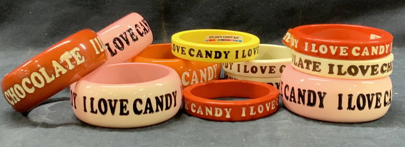 12 Dylans Candy Bar I Love Candy Bangles: Lot of 12 resin made bangles marked from Dylans candy bar. With text reading I love candy, I love chocolate. In colors of red, pink, yellow and white. 5 bangles 1.5 inches thick and 7 at 0.75 inch thi