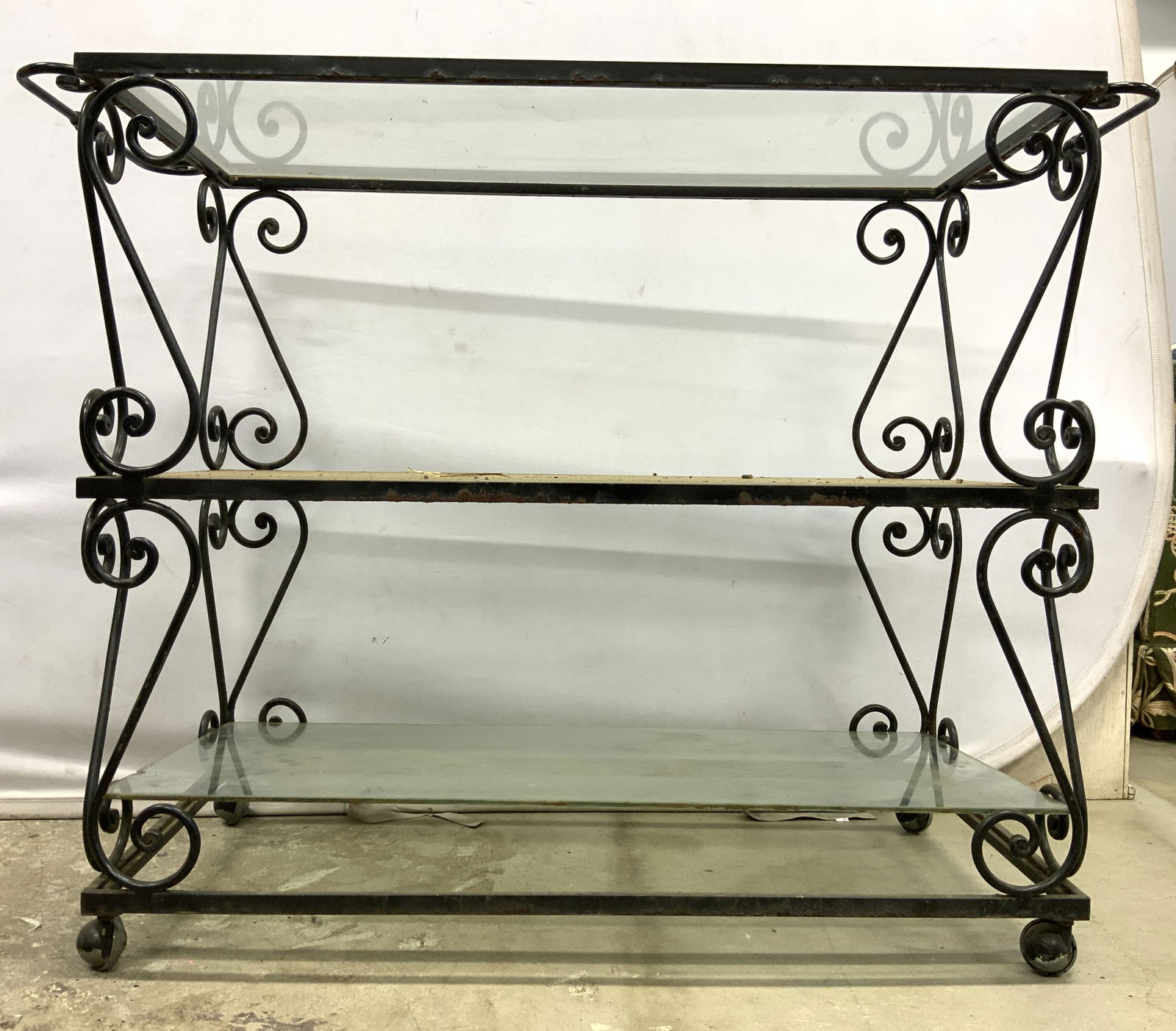 Vintage Iron & Glass 3 Tier Bar Cart: Bar cart is vintage. Frame appears to possibly be iron. Piece has 3 glass tiers. Frame has s curl structures & handles on each side. Cart has 4 wheels. Measures approx 42 inches long 33 inches tall 18