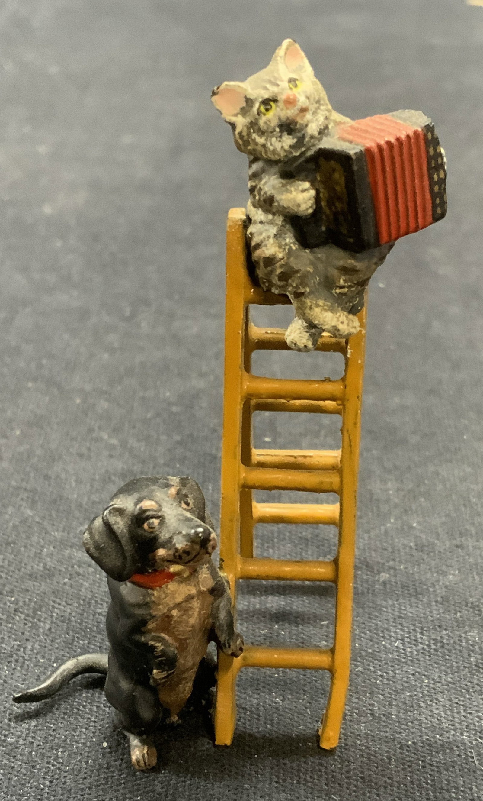 Vintage Enameled Metal Cat & Dog Figural: Vintage enameled Metal figurine. Cat with accordion and dog on ladder. Measures approx. 1.25 x 1.25 x 2.25 inches. Some surface wear including scratching observed. Cat figurine, dog figurine, cat and 