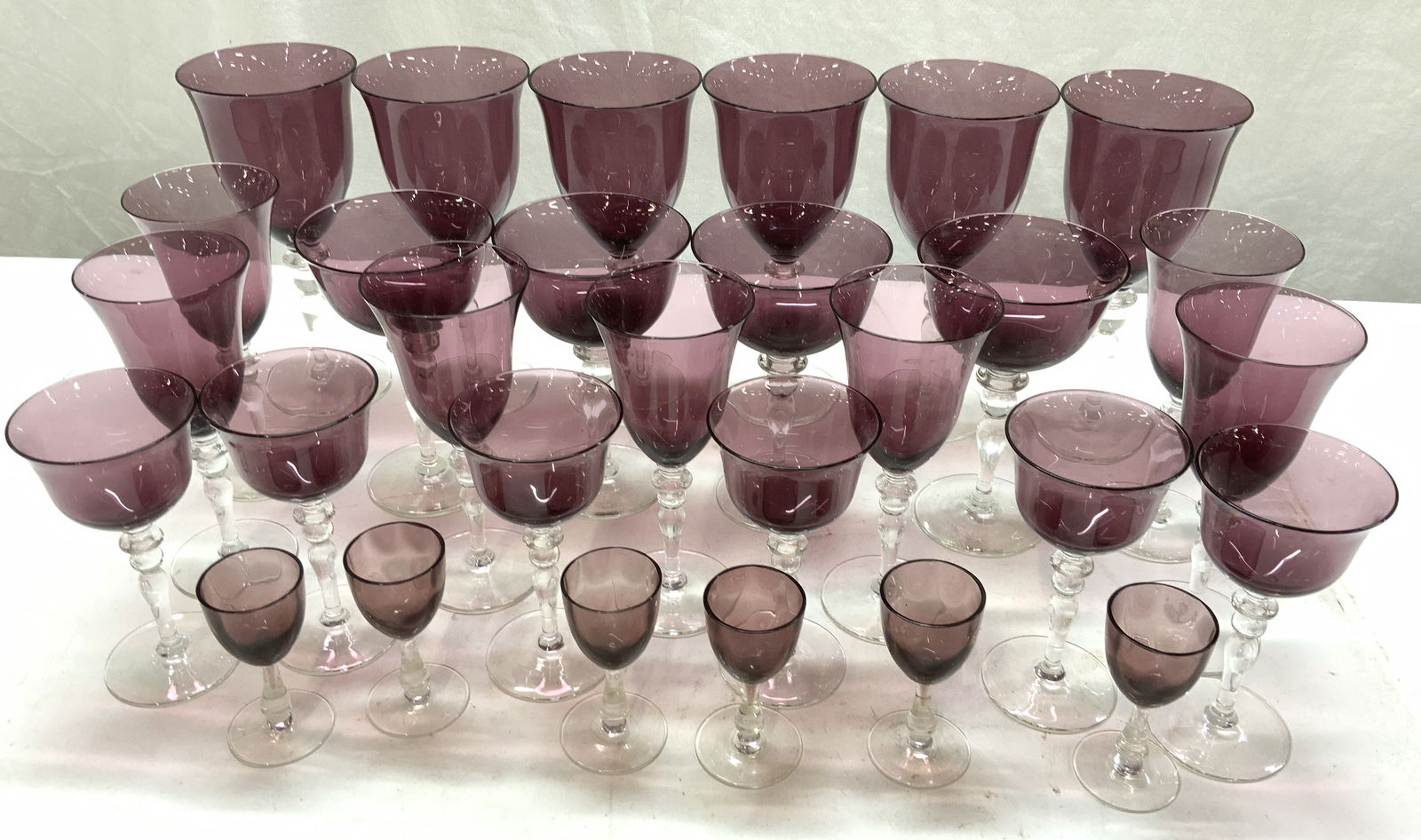 Bohemian Amethyst Blown Crystal Stemware Set 29: Amethyst blown crystal goblets with clear crystal stems. 5 different sizes and shapes. Largest goblet measures 7.75 x 3.75 in. W. Wine glasses, champagne coupe, aperitif and cordial glasses, set of 29