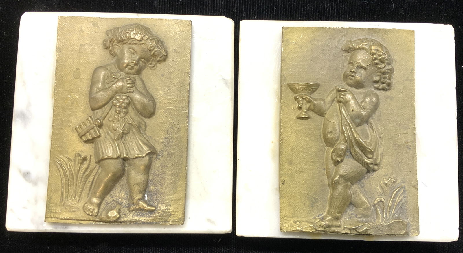 Marble & Gilt Brass Neoclassical Plaques, 2: Embossed gilt brass plaques on top of square marble bases. Feature neoclassical children with wine cup and grape bunch. Use as paperweights. Or up cycle in another way. Bases have drilled holes, likel