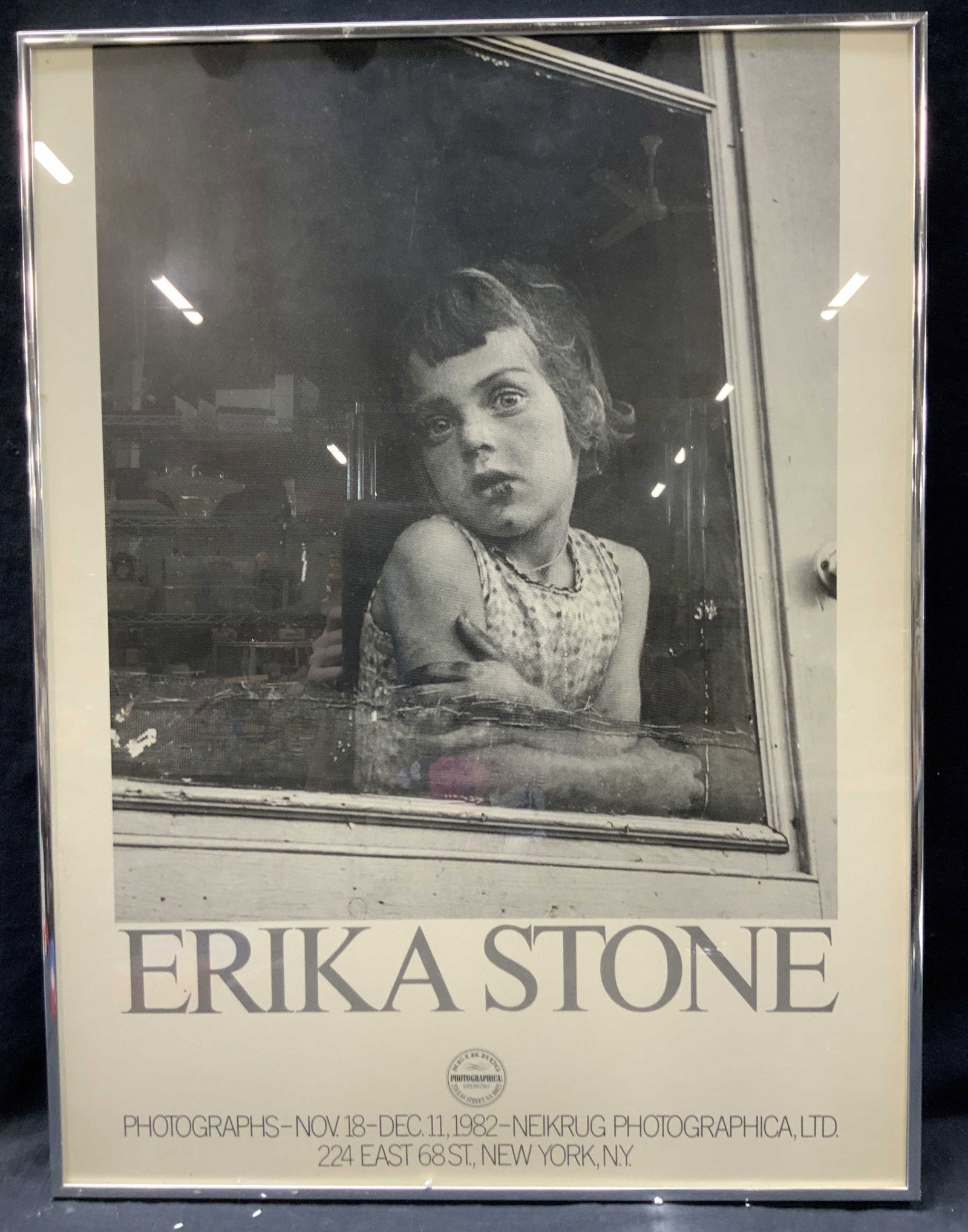 Erika Stone Photography Exhibition Advert: Exhibition advert for Erika stone, reading photographs nov,18-Dec 11 1982 Neikburg Photographica. Depicts a black and white image of a young girl looking out of a window. Framed in a silver toned meta