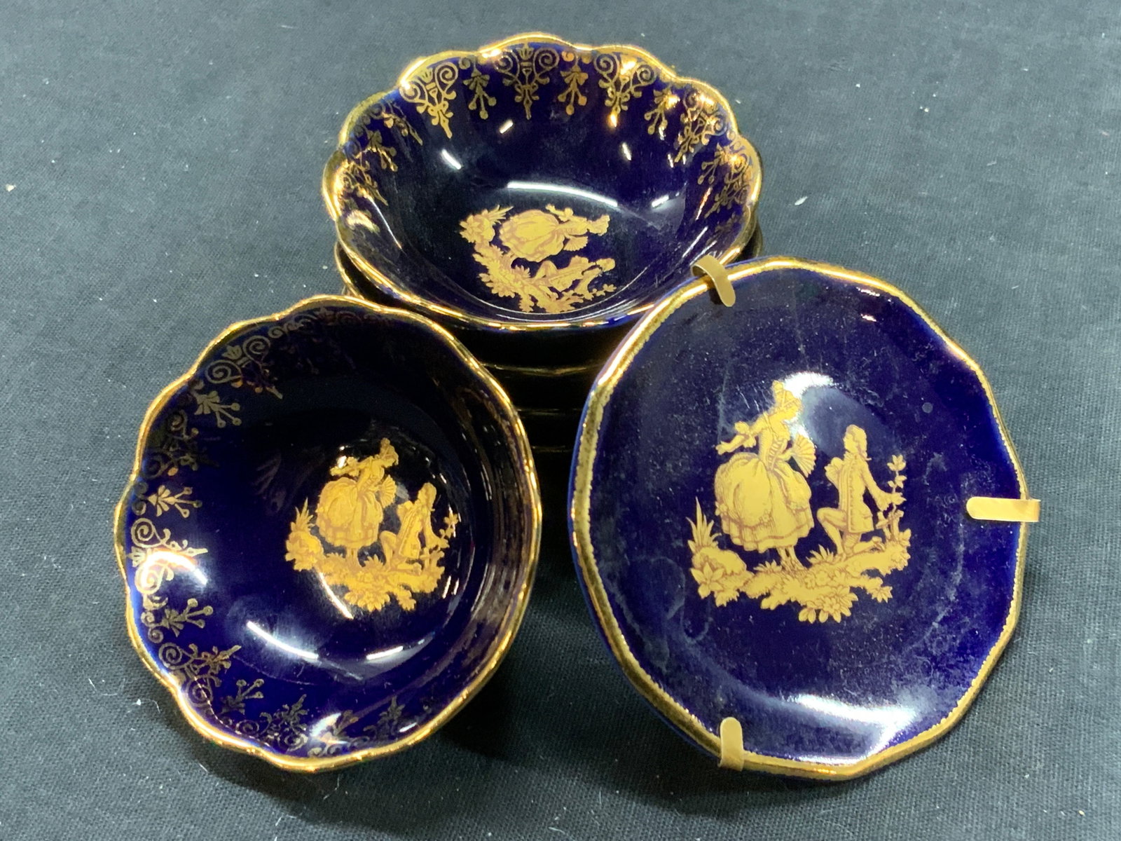 6 Limoges Cobalt & Gilt Porcelain Trinket Dishes: Set of 6 Limoges France porcelain trinket dishes, 5 trinket bowls with gilt rims on the cobalt exterior and images of a man and woman in gold in the centers, approx 1 inch tall and 2.5 inch diameter. 