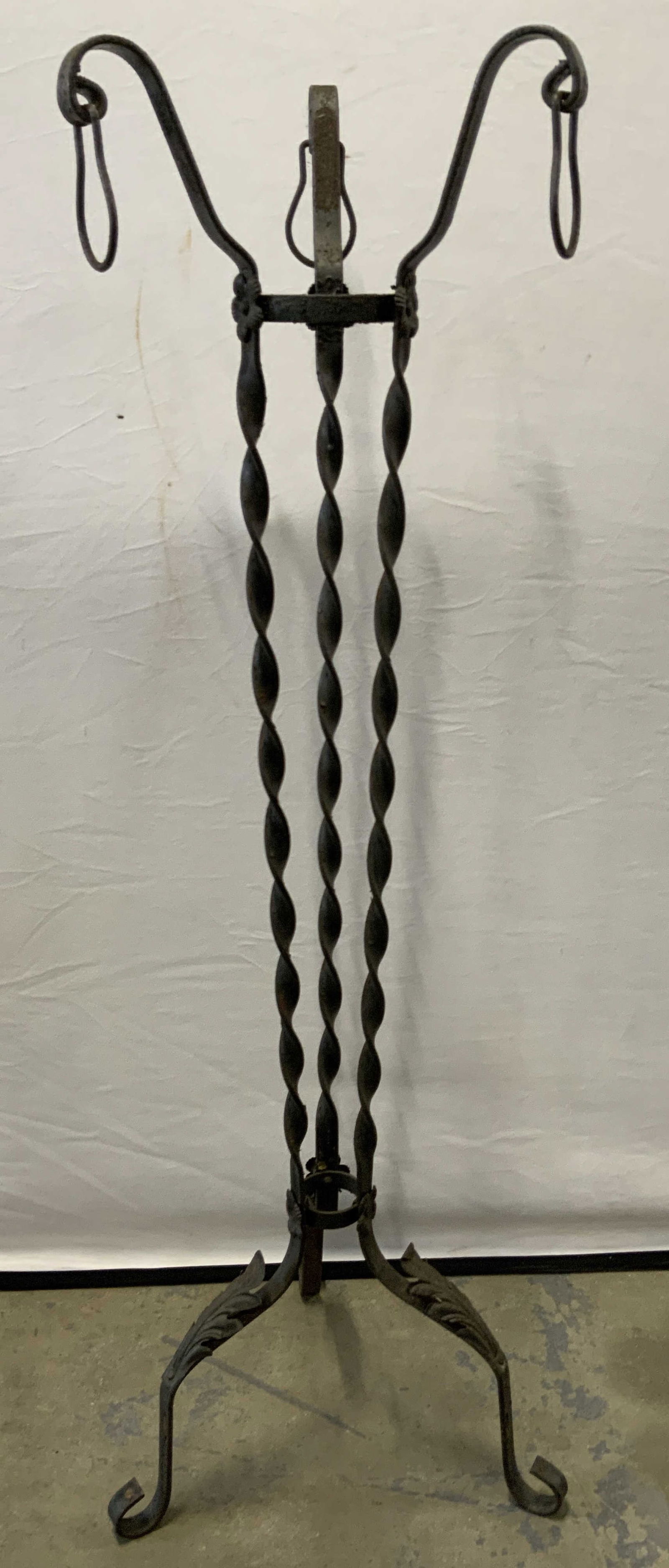 Vintage Black Wrought Iron Plant Stand: A vintage black wrought metal, possibly iron, plant stand. Dangling rings to the three arms, raised floral motifs, twisted metal accents, and scroll feet to the piece. Measures approx. 43H x 11.5W x 1